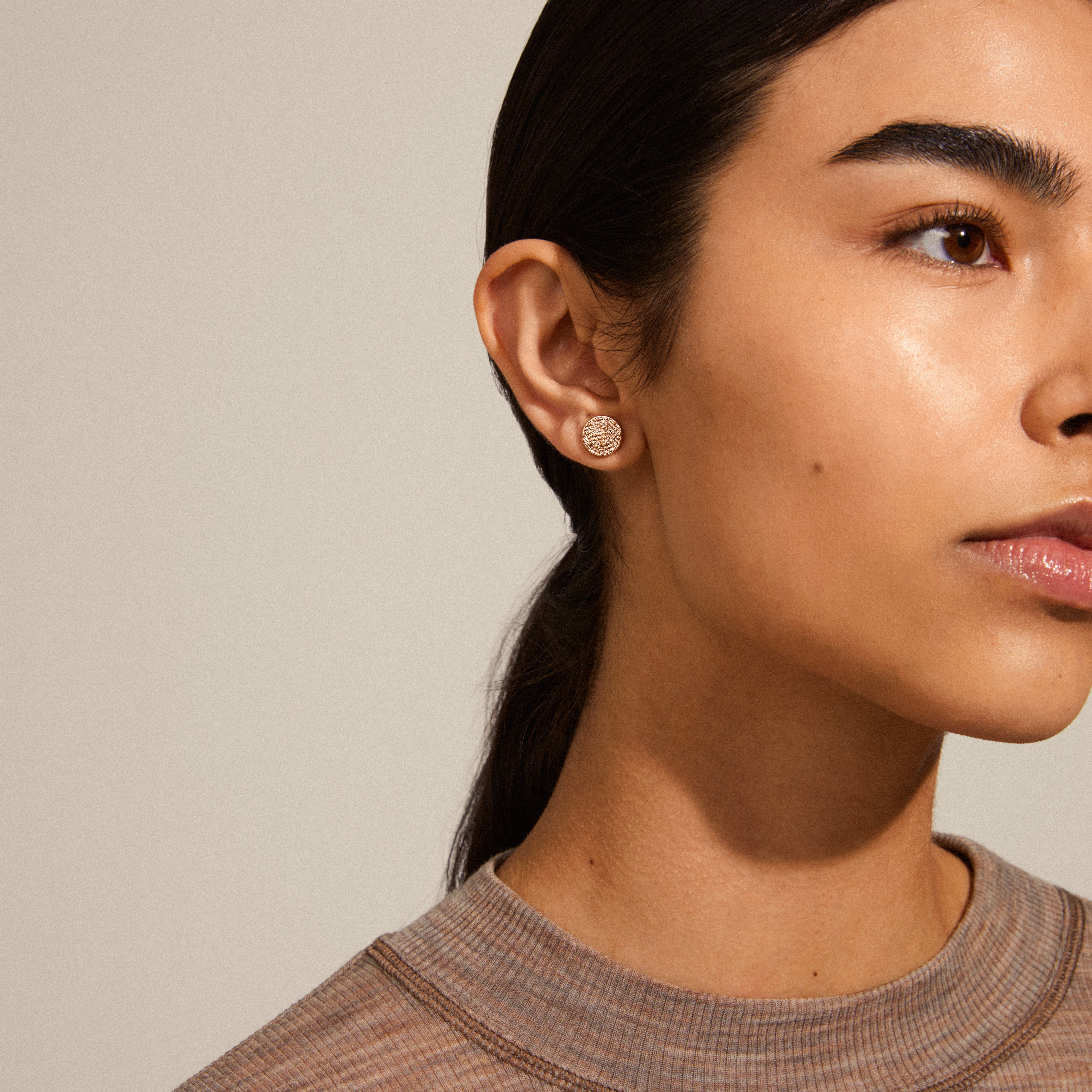 Woman wearing WYNONNA rustic earrings, rosegold-plated with a shiny finish and rustic pattern, showcasing their edgy yet elegant style.