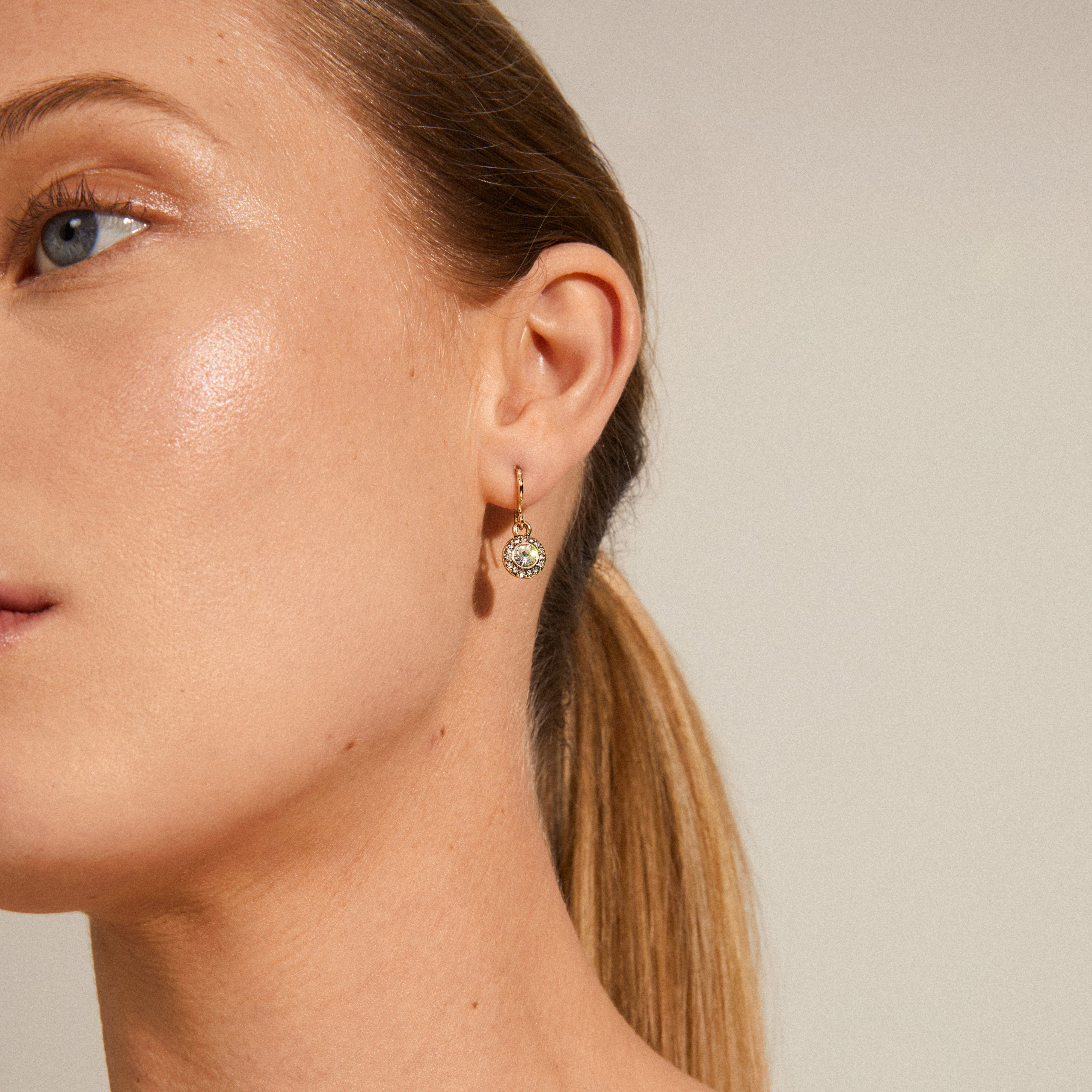 CLEMENTINE crystal earrings gold-plated, featuring a large central crystal surrounded by smaller stones, elegantly showcased on a woman with a ponytail.