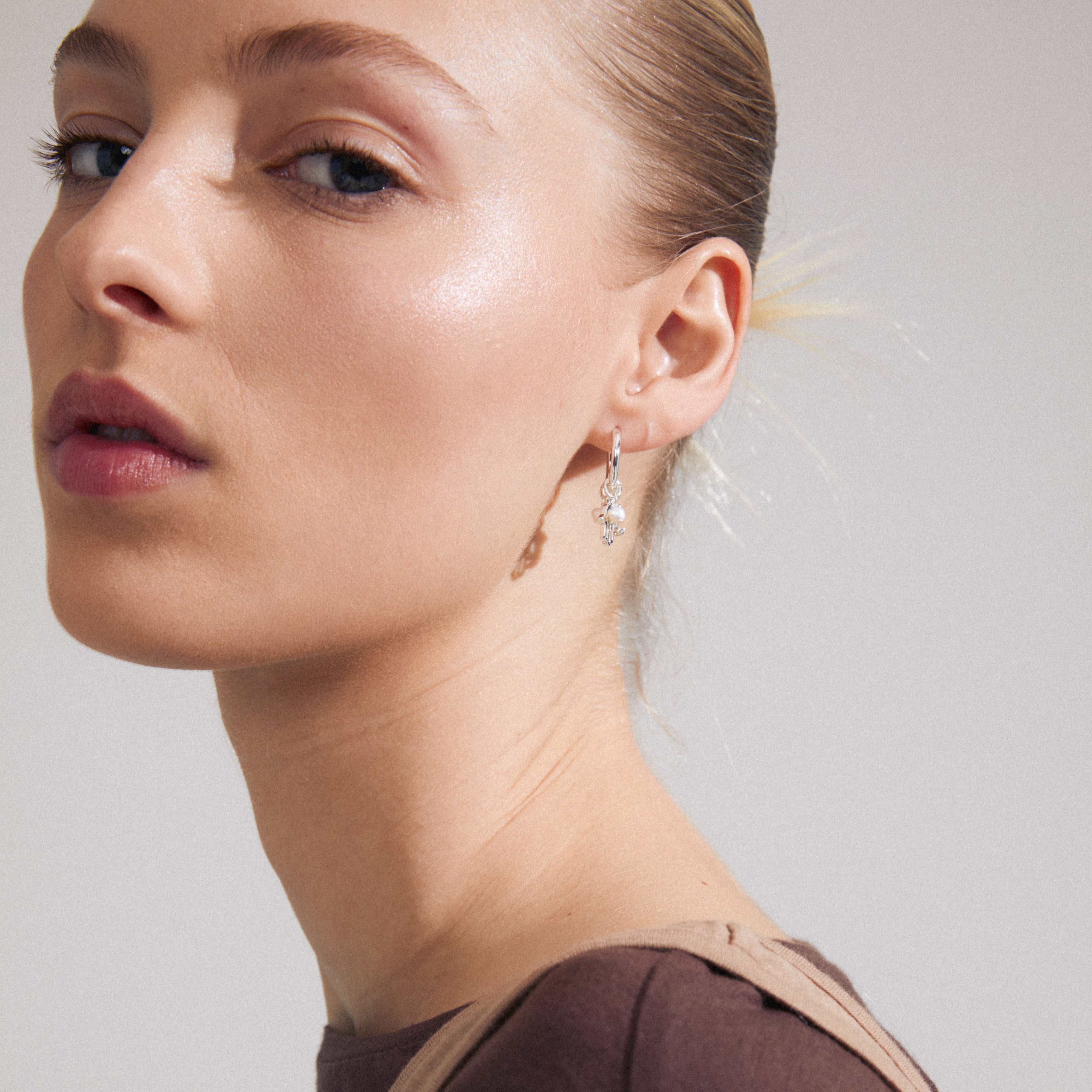 PRUCENCE earrings silver-plated, featuring charming hoops with moon and Hamsa symbols, adorned with tiny freshwater pearls and Preciosa crystals, worn by a woman.