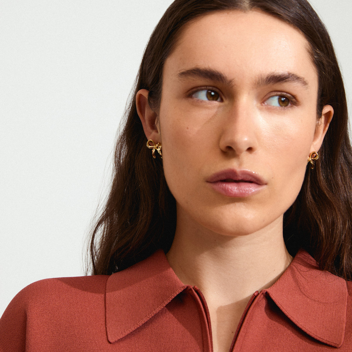 CASSIAN earrings gold-plated, featuring a stylish bow design, worn by a woman looking to the side, highlighting Pilgrim's handmade, trendy jewellery craftsmanship.