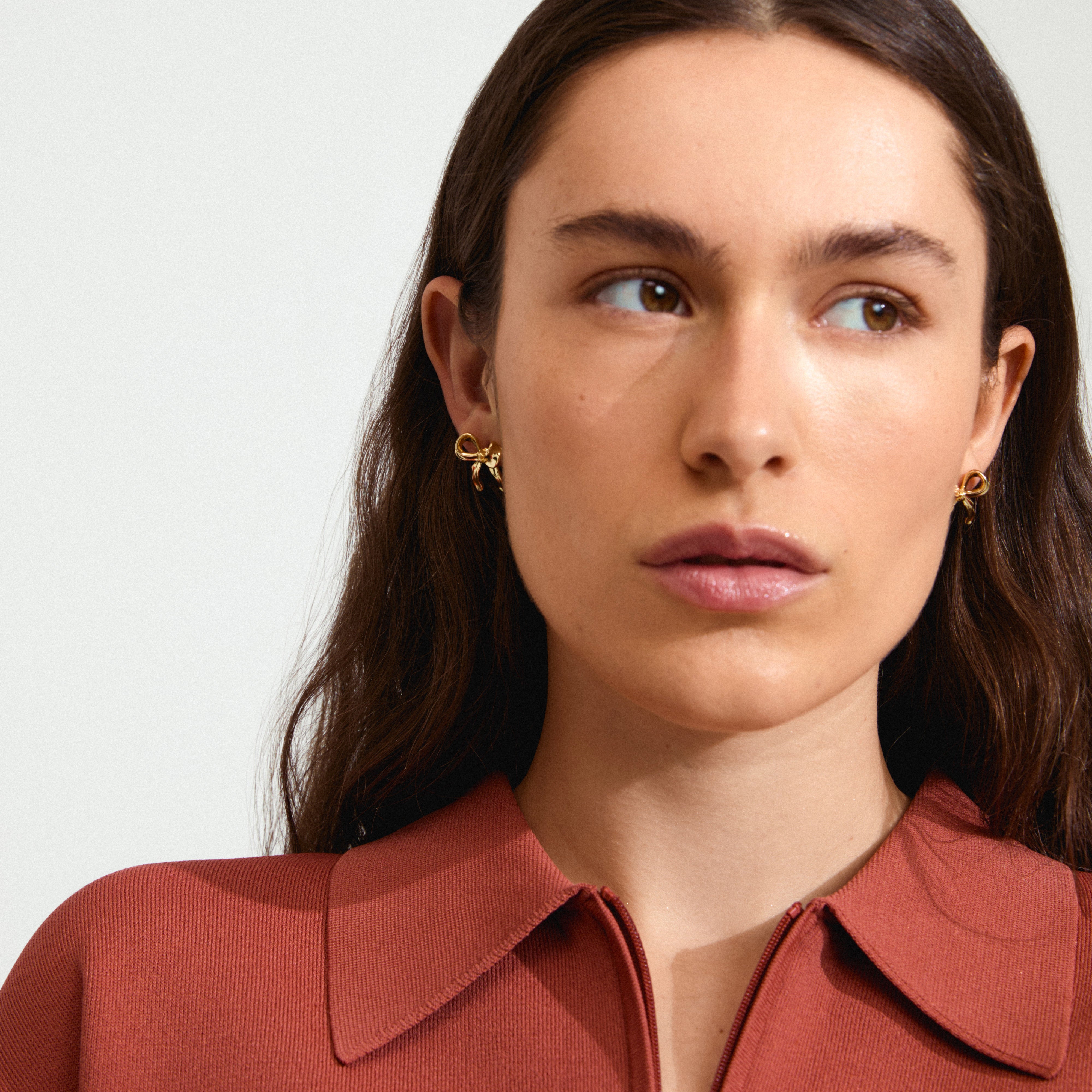 CASSIAN earrings gold-plated, featuring a stylish bow design, worn by a woman looking to the side, highlighting Pilgrim's handmade, trendy jewellery craftsmanship.