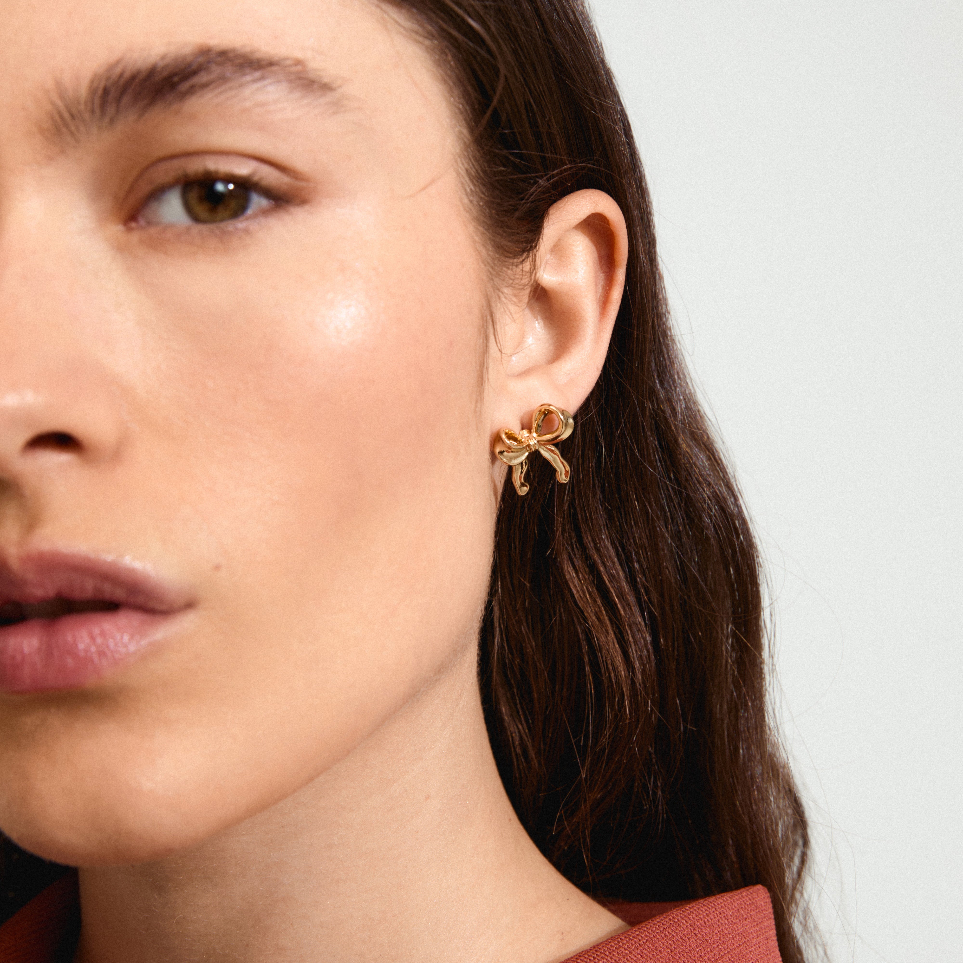 CASSIAN earrings gold-plated on a woman's ear, featuring a stylish gold-plated bow design from Pilgrim's Classic collection, crafted with 96% recycled material.