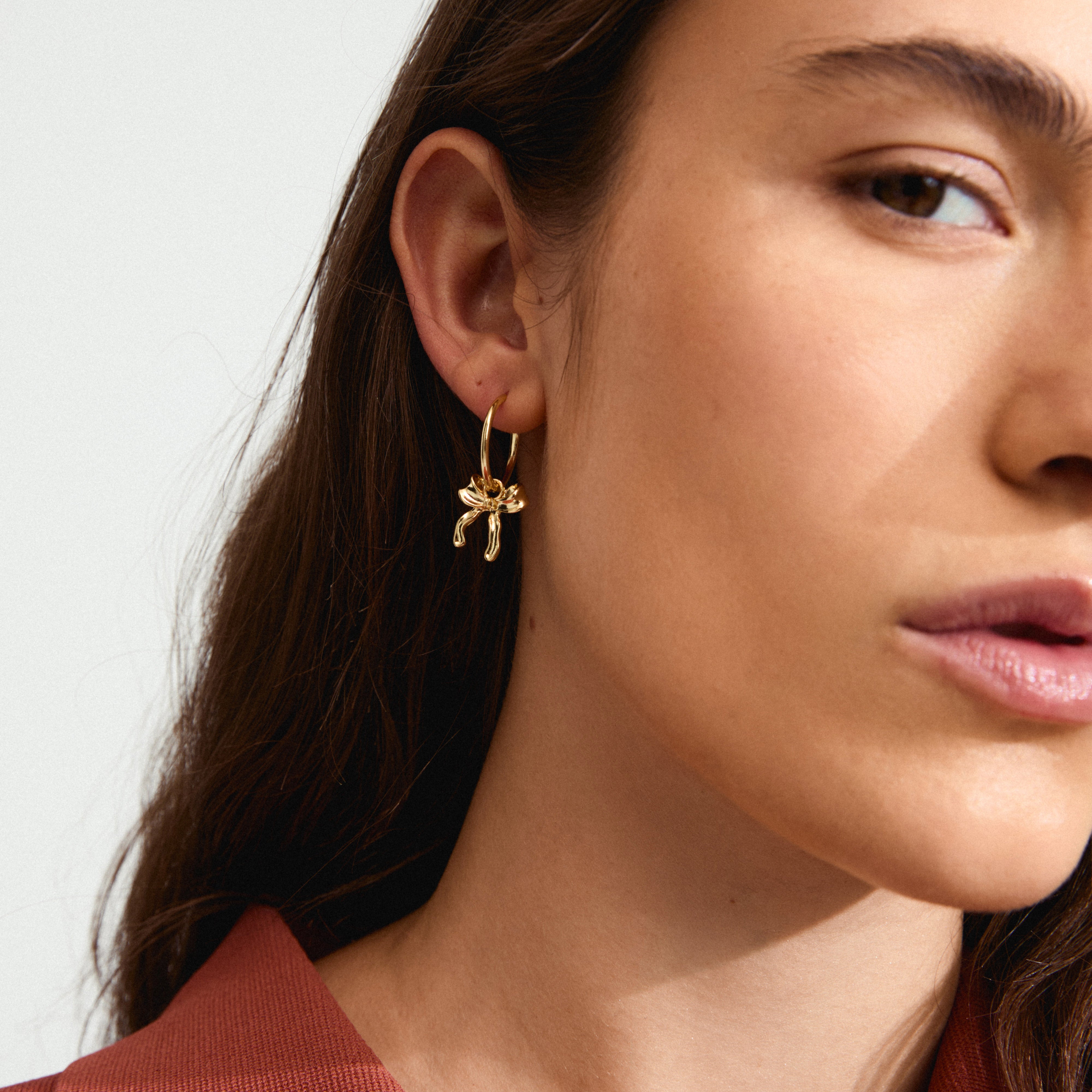 CASSIAN hoop earrings gold-plated with trendy bow pendants, worn by a woman, showcasing their elegant, effortless style. Perfect for everyday outfits and summer dresses.