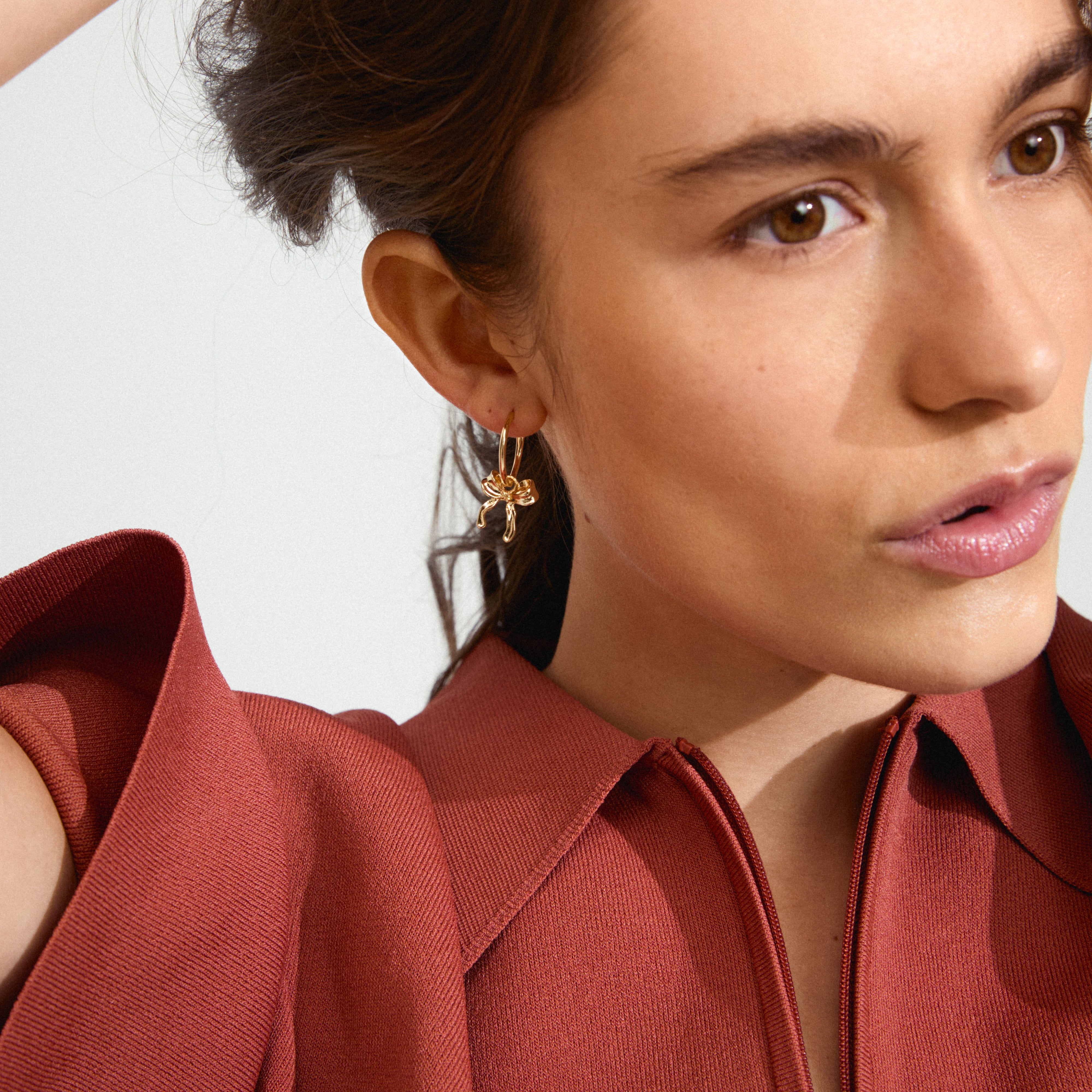 CASSIAN gold-plated hoop earrings with bow pendants worn by a woman, highlighting their trendy design and ease of use for stylish, everyday wear.