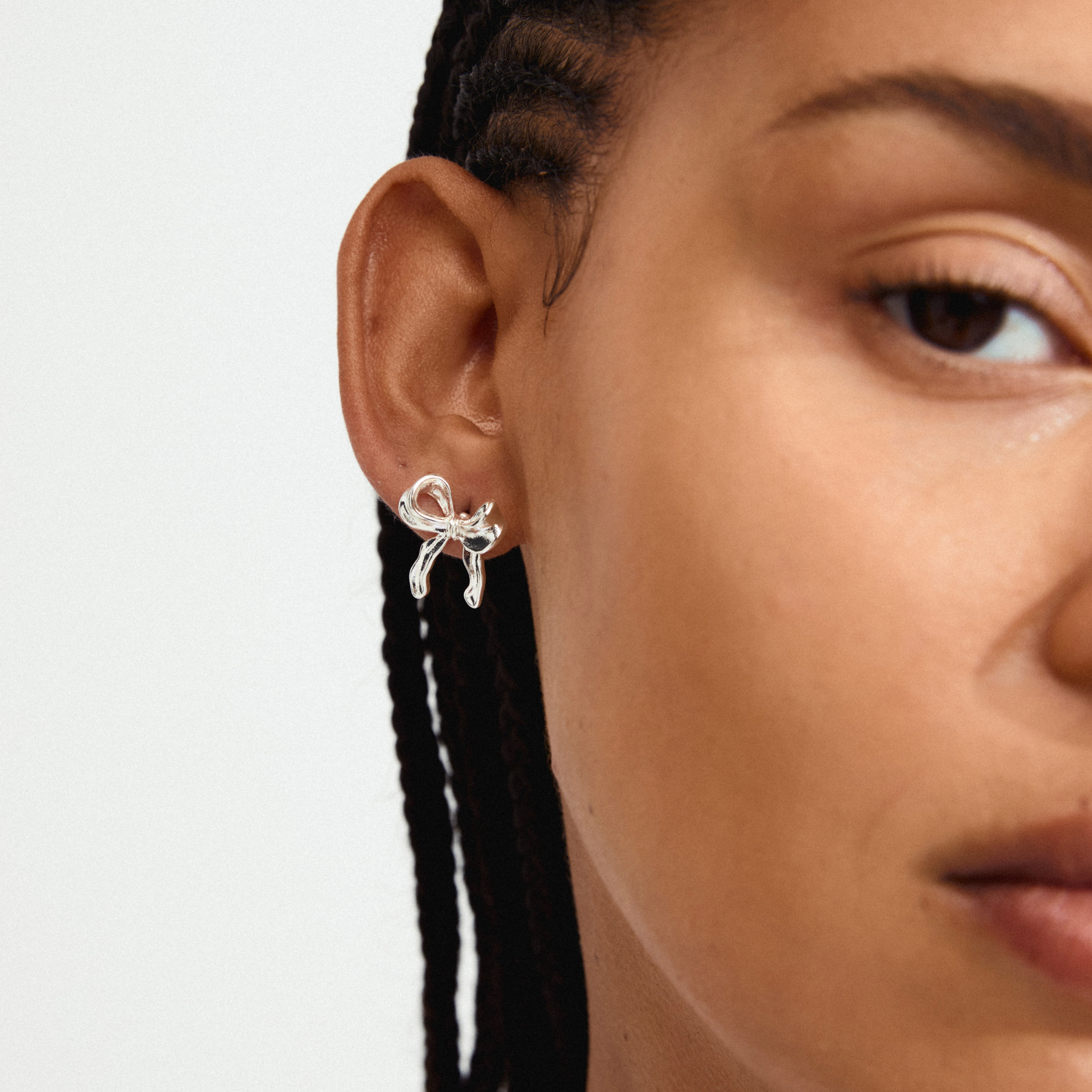 CASSIAN earrings silver-plated; close-up of a woman's ear adorned with silver-plated bow earrings, showcasing Pilgrim's trendy, sustainable, and timeless design.