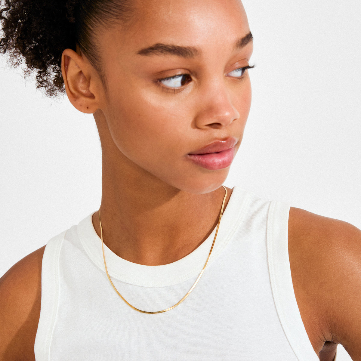 Young person wears the NIKITA necklace gold-plated, a sleek herringbone chain that elegantly catches light, embodying timeless style and trendy, Scandinavian design.