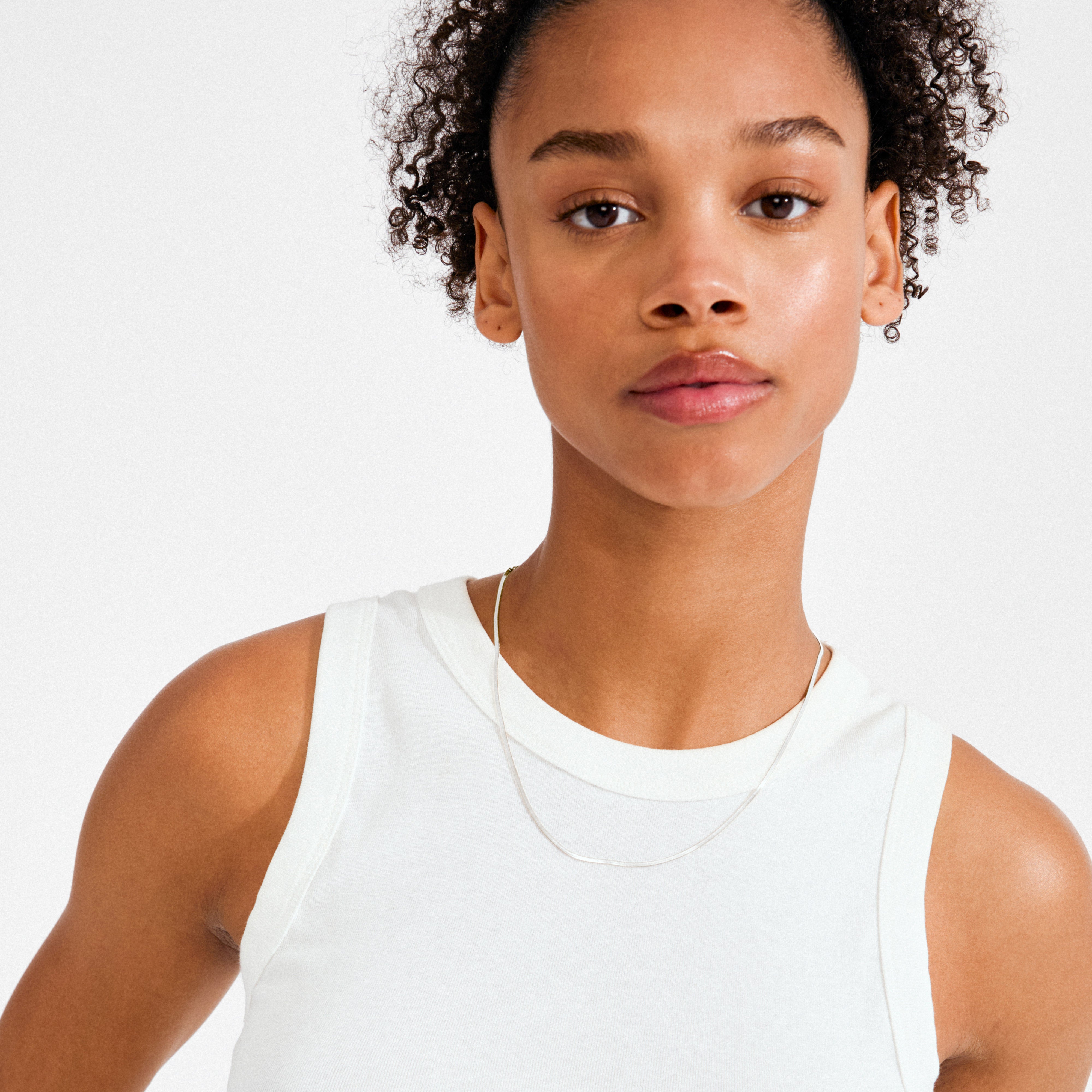 Young person wearing Pilgrim’s NIKITA necklace silver-plated, a sleek herringbone chain, elegantly draped, adding a genderless edge to their look against a plain background.