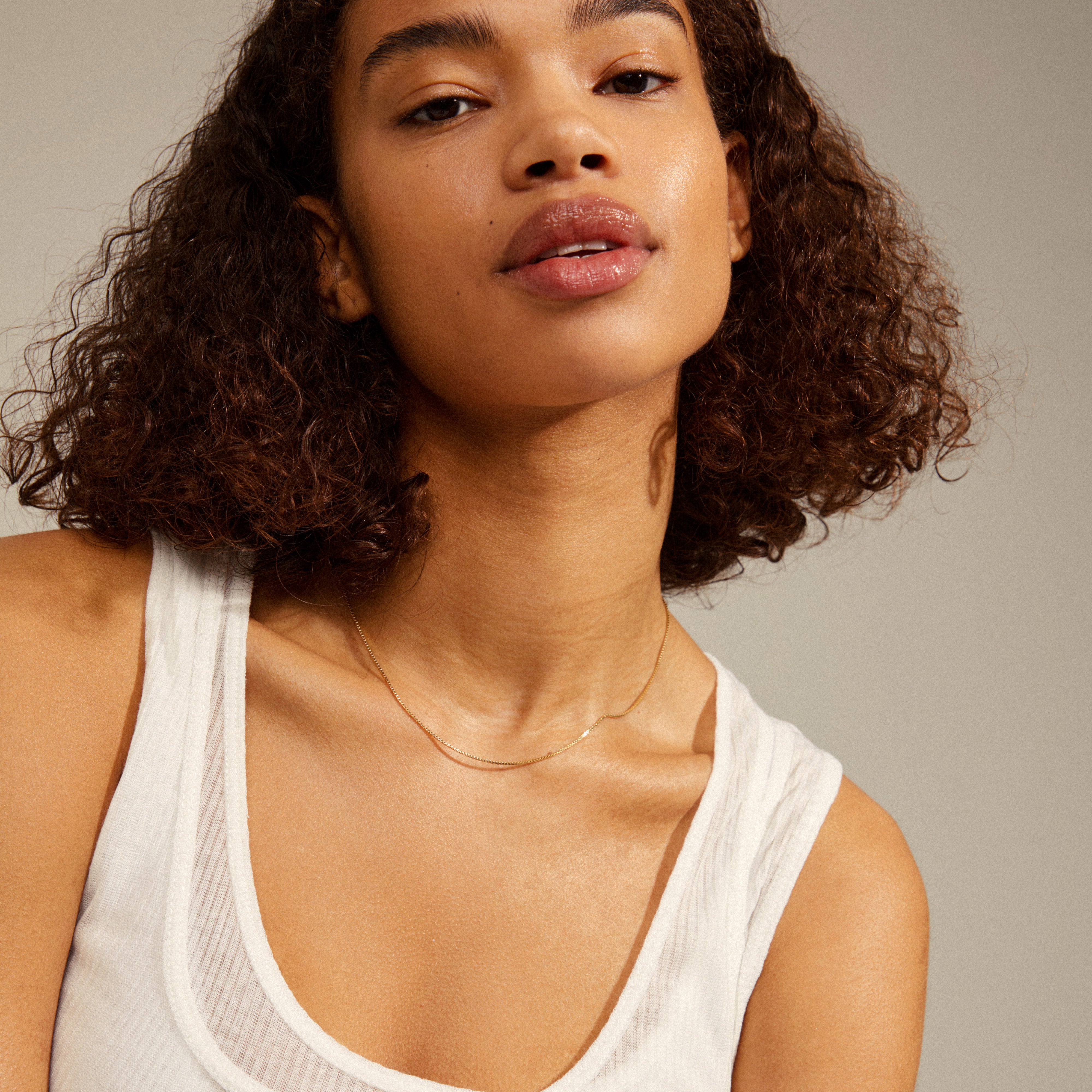 NANCY necklace 45 cm gold-plated on a woman with curly hair wearing a white tank top, highlighting its versatility for layering or adding a pendant.
