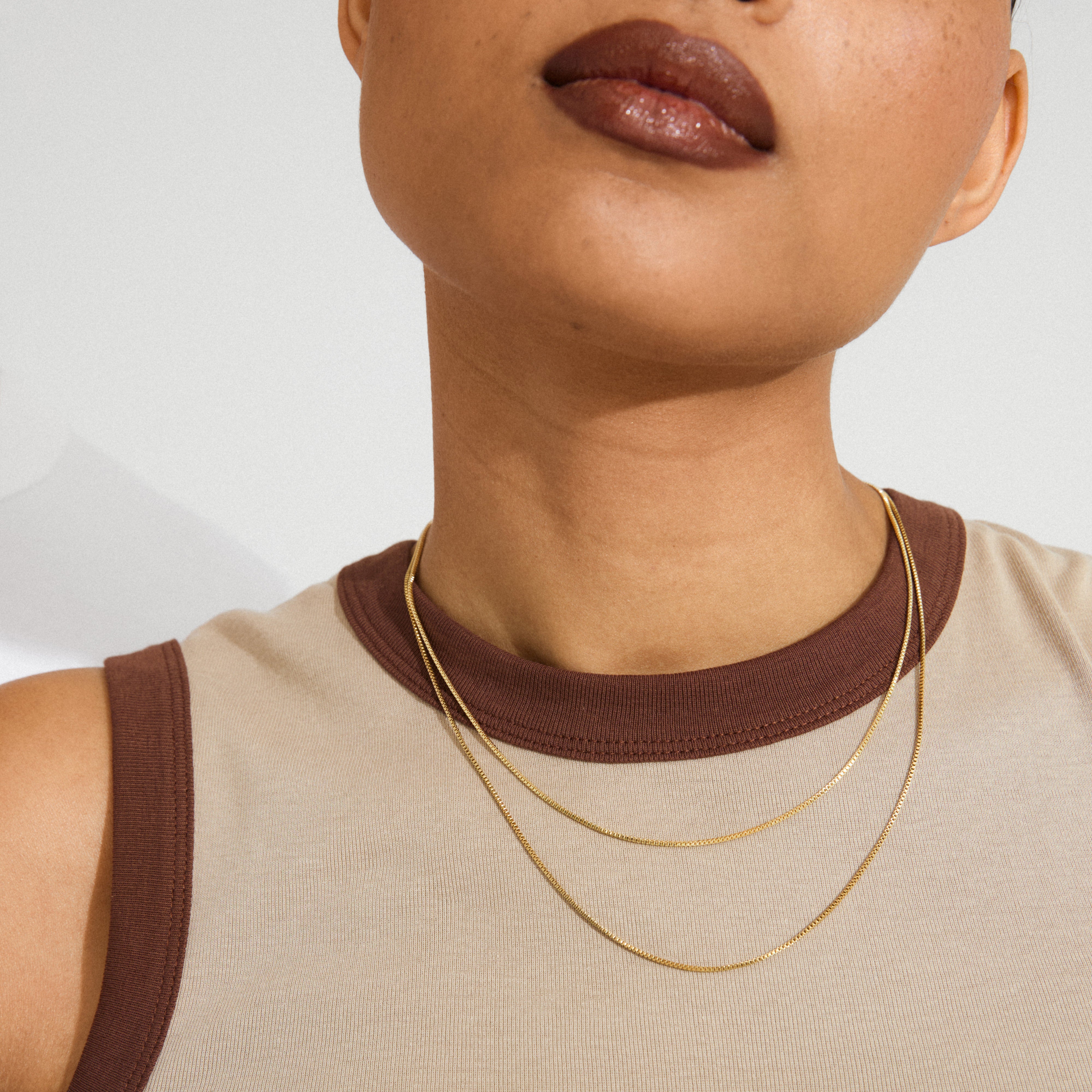 Person wearing a sleeveless top, showcasing the Pilgrim NANCY necklace 45 cm gold-plated, layered elegantly with another chain around their neck.