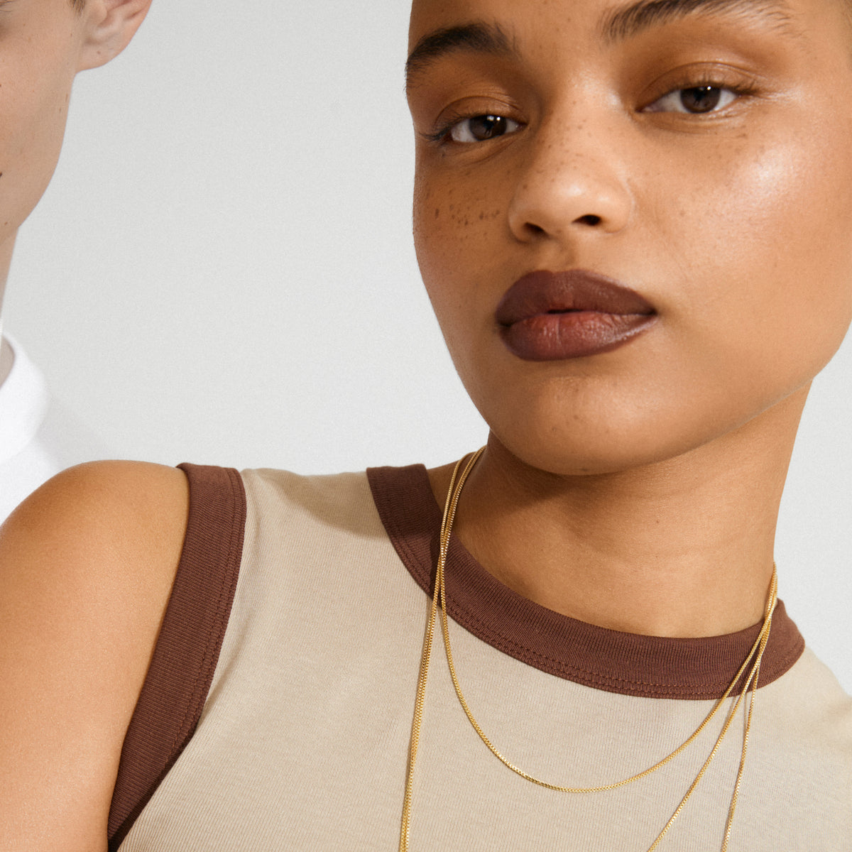 Young woman wearing the NANCY necklace 80 cm gold-plated, elegantly draped around her neck, paired with a beige ribbed tank top showcasing minimalist Scandinavian style.