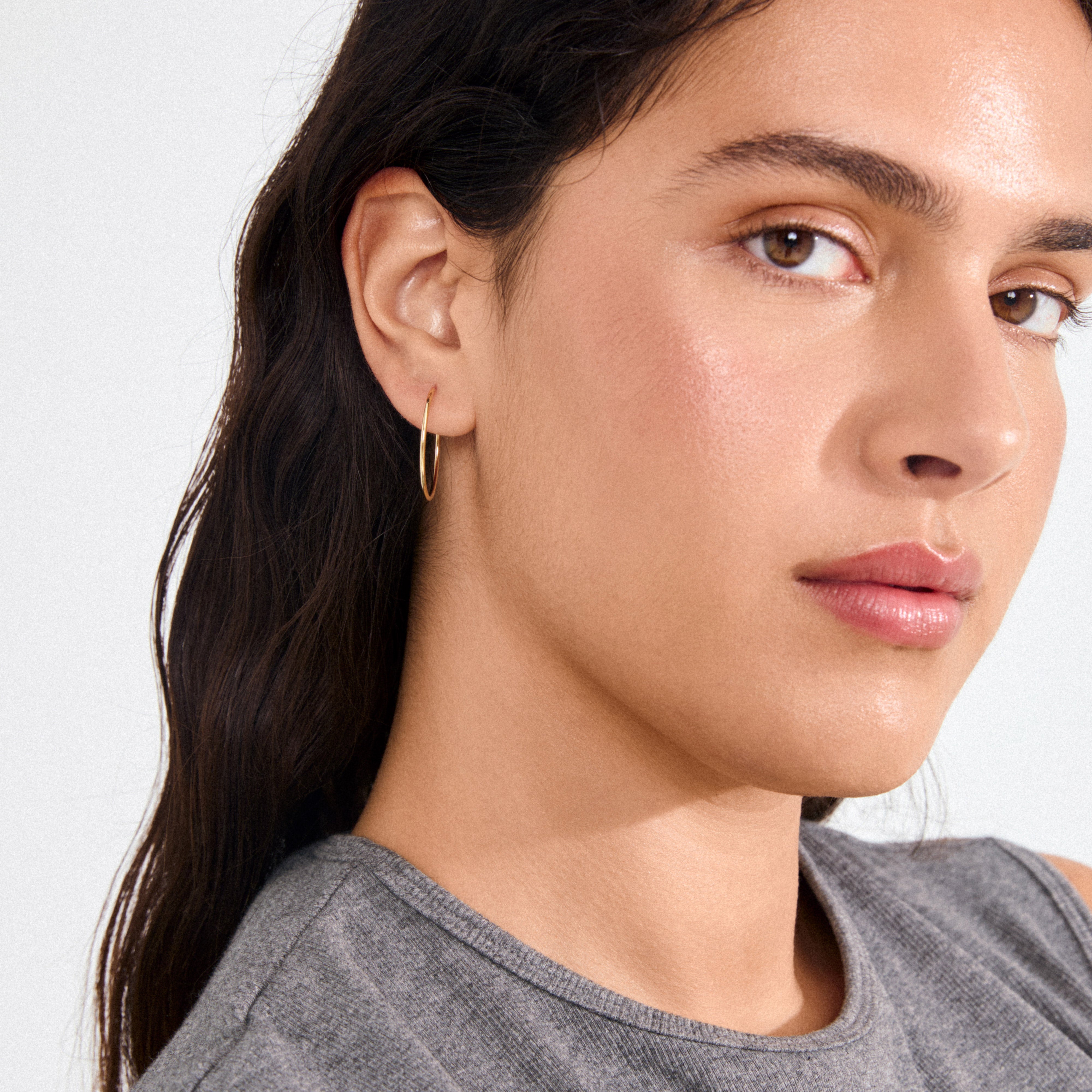 Young woman wearing SANNE medium hoop earrings gold-plated, showcasing their timeless elegance and effortless style, perfect for everyday wear or layered with other jewelry pieces.
