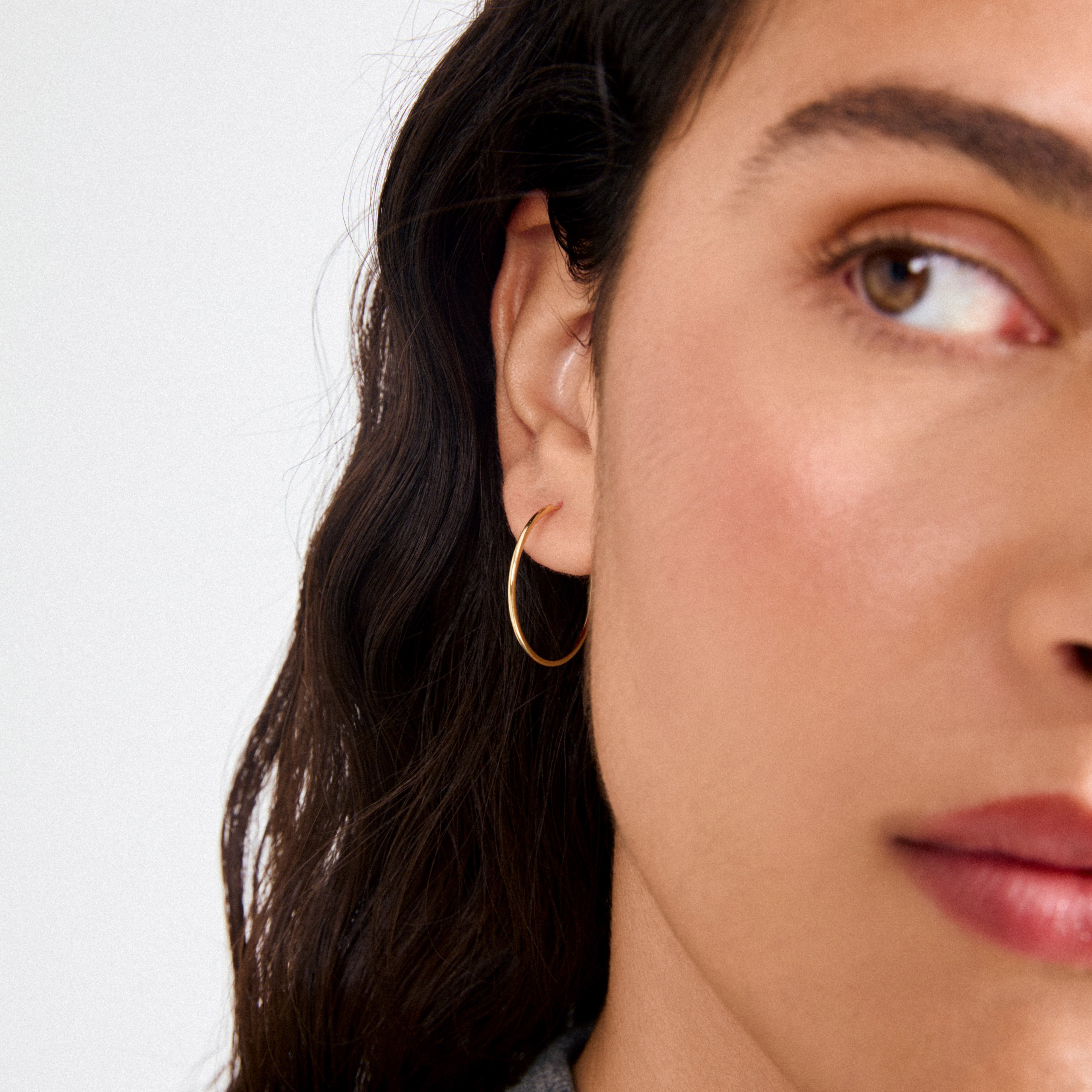 Close-up of SANNE medium hoop earrings gold-plated, shown on a person with medium skin tone and wavy hair, highlighting their timeless and stylish design.