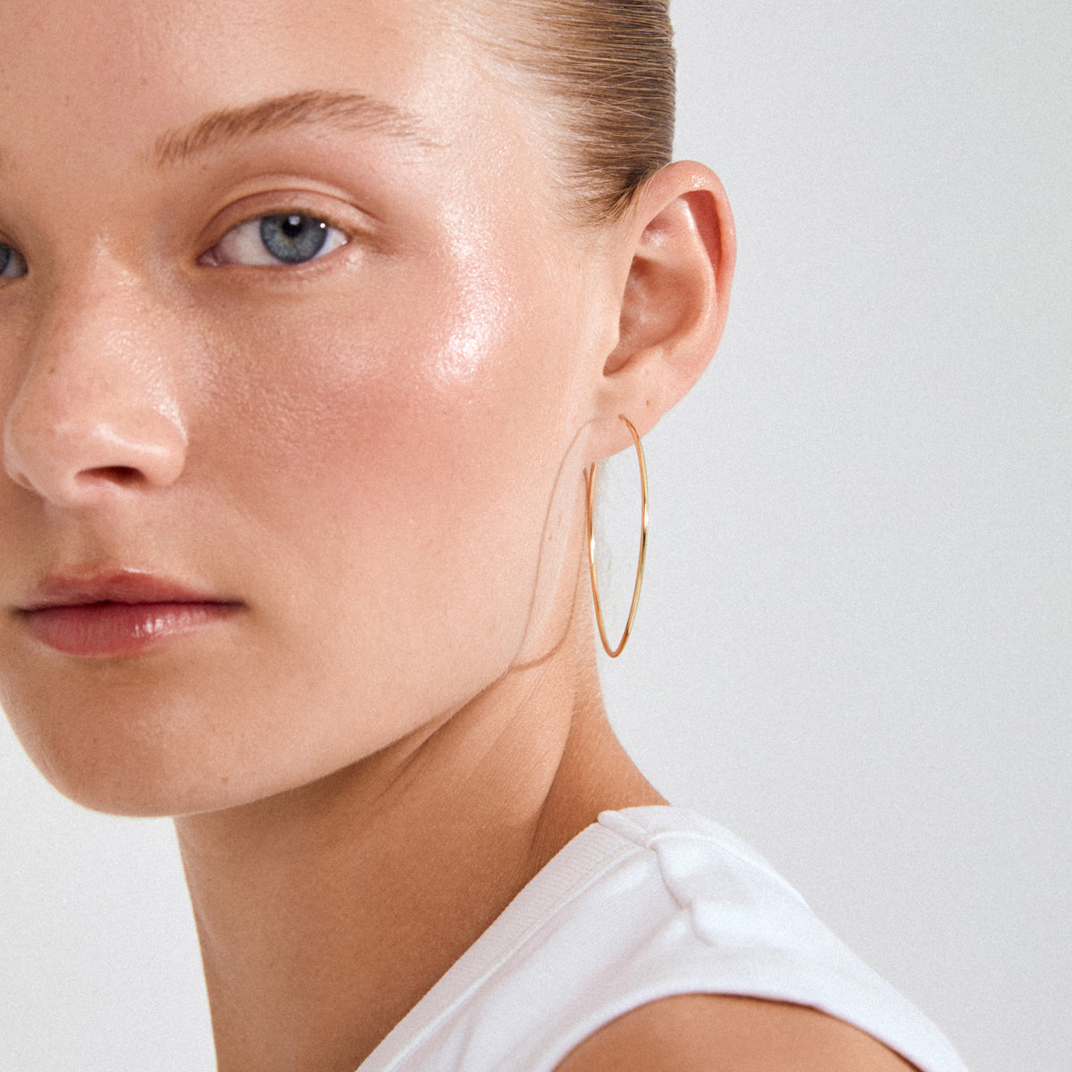 Close-up of a young woman wearing SANNE large gold-plated hoop earring, showcasing its timeless elegance and versatility against her smooth skin and simple white top.