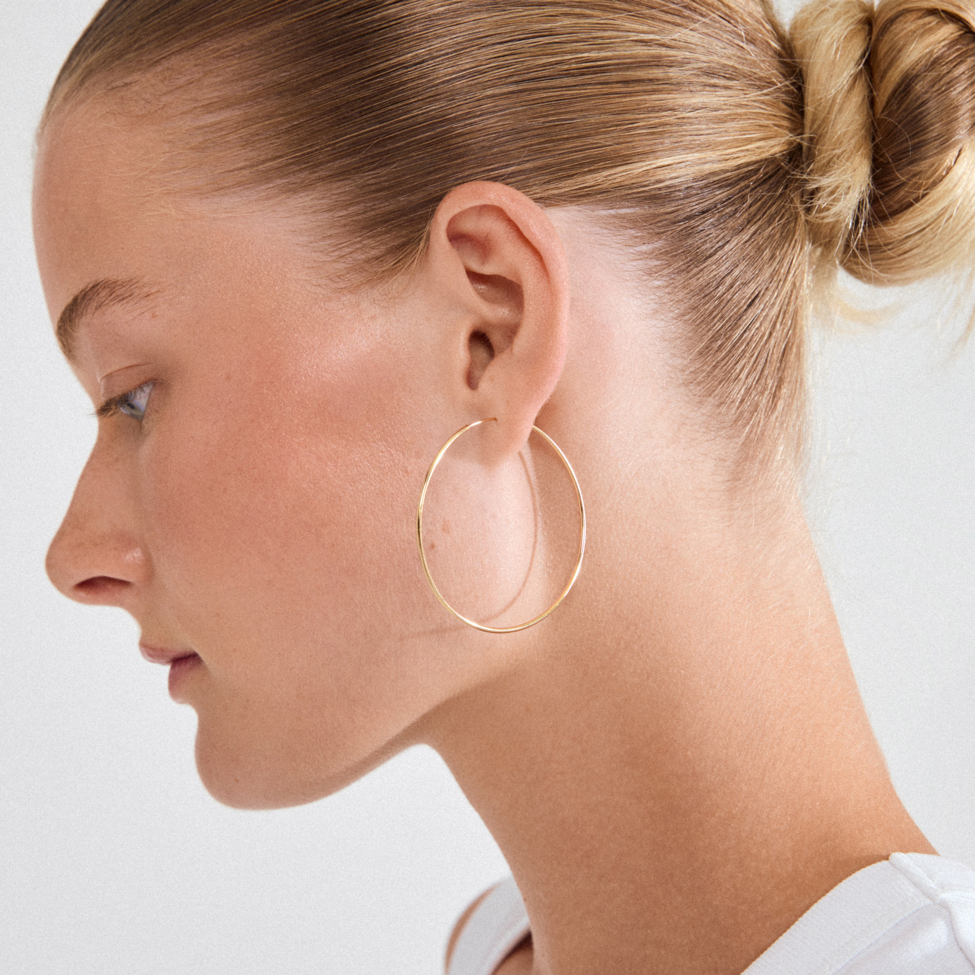 Profile of a woman wearing a SANNE large hoop earring, gold-plated, 45 mm, showcasing its classic elegance and timeless style.
