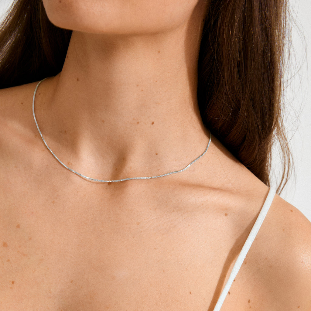 Woman wearing the NANCY necklace 45 cm silver-plated, a fine chain from Pilgrim, shown close-up on her neck, paired with a white narrow-strap top.