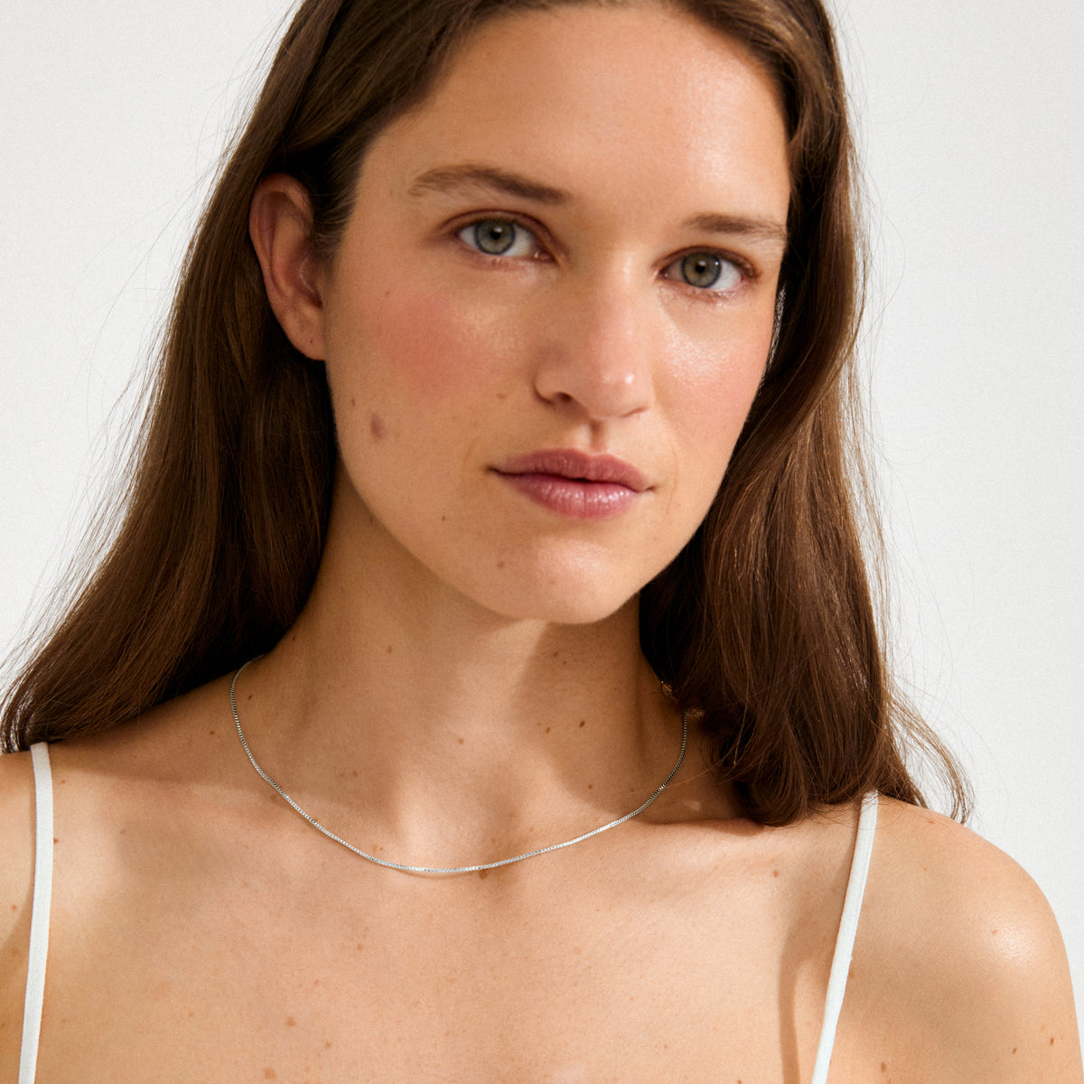 Young woman wearing the NANCY necklace, a 45 cm silver-plated Venezia chain, styled simply with a white spaghetti-strap top for a minimalist, elegant look.