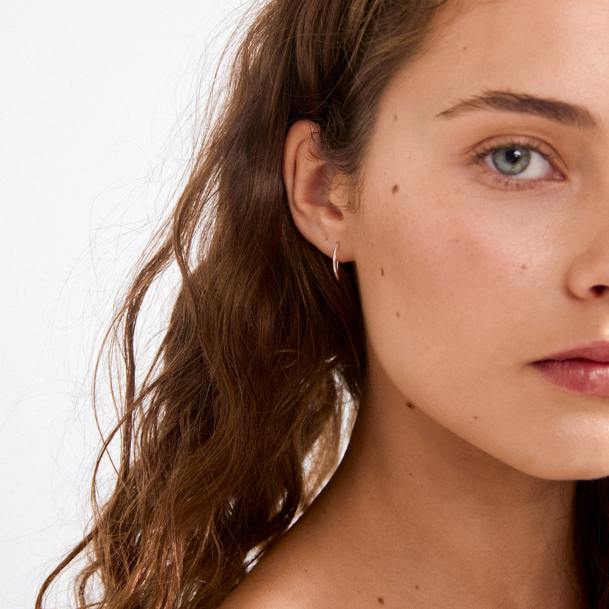 Young woman wearing SANNE mini hoop earrings, silver-plated, showcasing their elegant and versatile design, perfect for enhancing any look with a timeless touch.