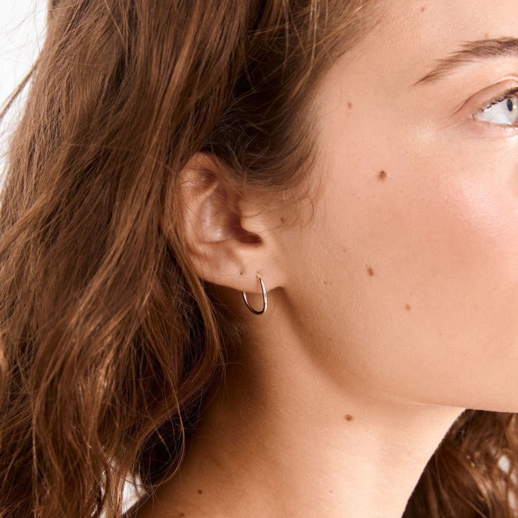 Close-up of a person's ear wearing SANNE mini hoop earrings, silver-plated, showcasing a sleek, timeless design suitable for both casual and festive styles.