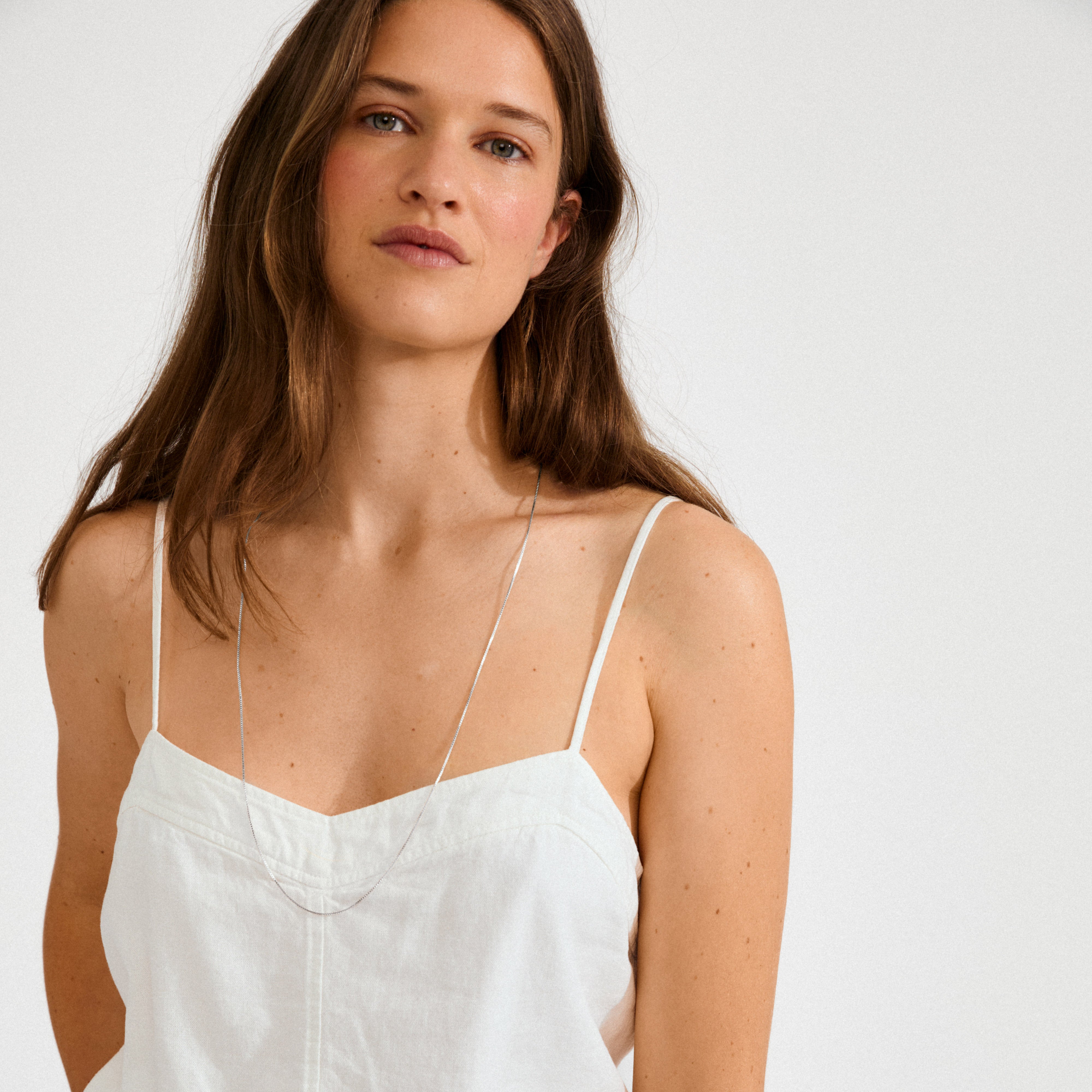 Young woman wearing the NANCY necklace, 80 cm silver-plated, with a minimalist style. The fine chain complements her simple white camisole, embodying Scandinavian elegance.