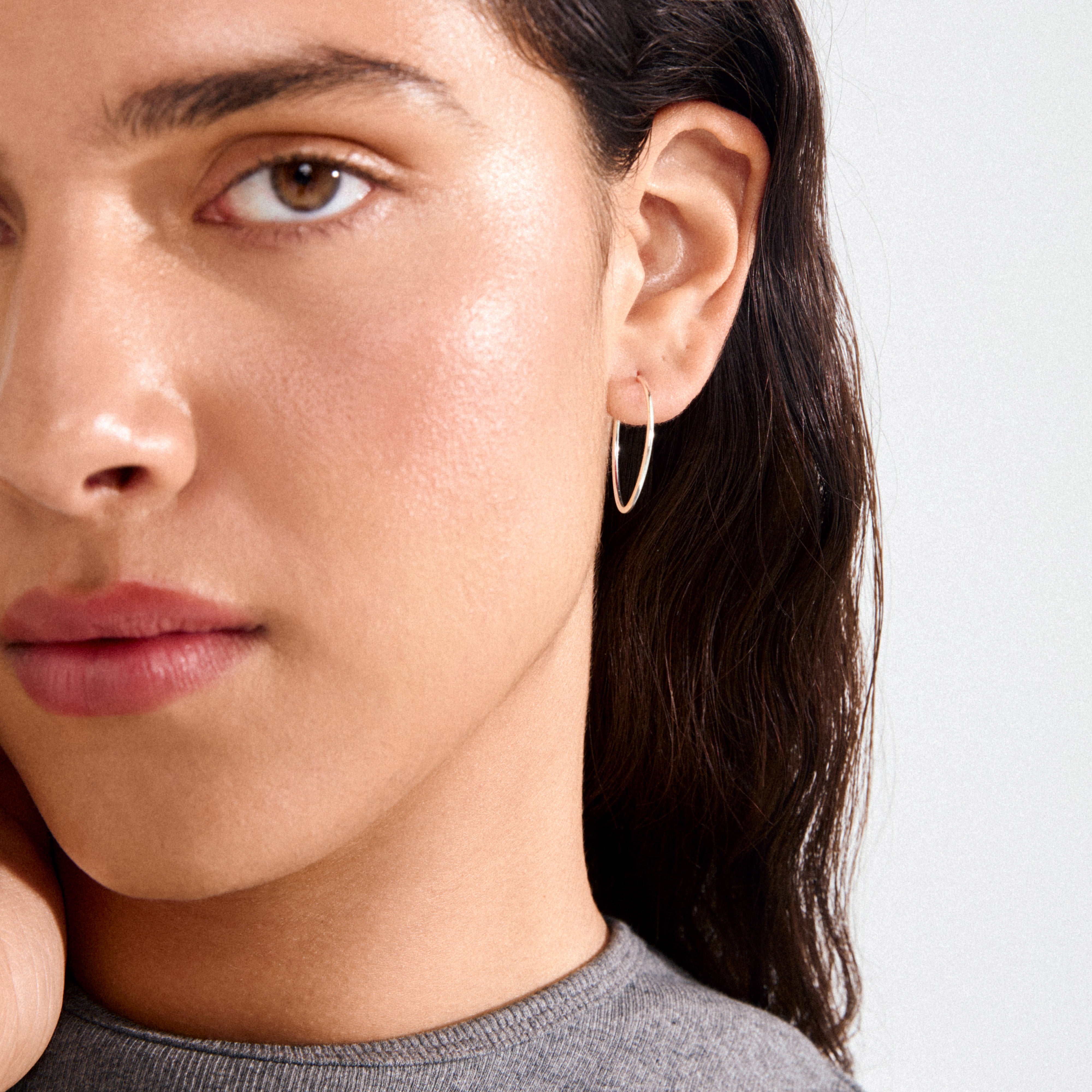 Young woman wearing SANNE medium hoop earrings, silver-plated, showcasing timeless elegance and everyday style with a close-up of her face and neck.
