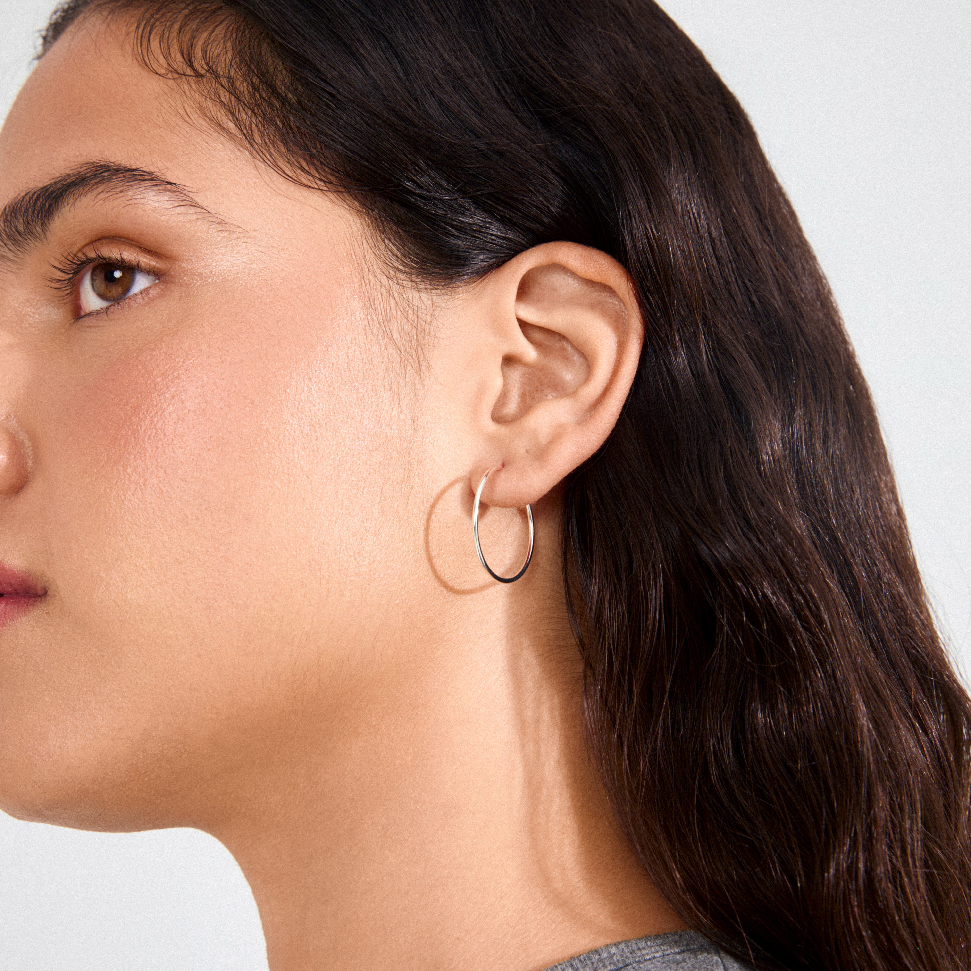 Profile view of a woman's ear wearing SANNE medium hoop earrings, silver-plated, showcasing timeless elegance and versatile style from Pilgrim's Danish jewelry collection.
