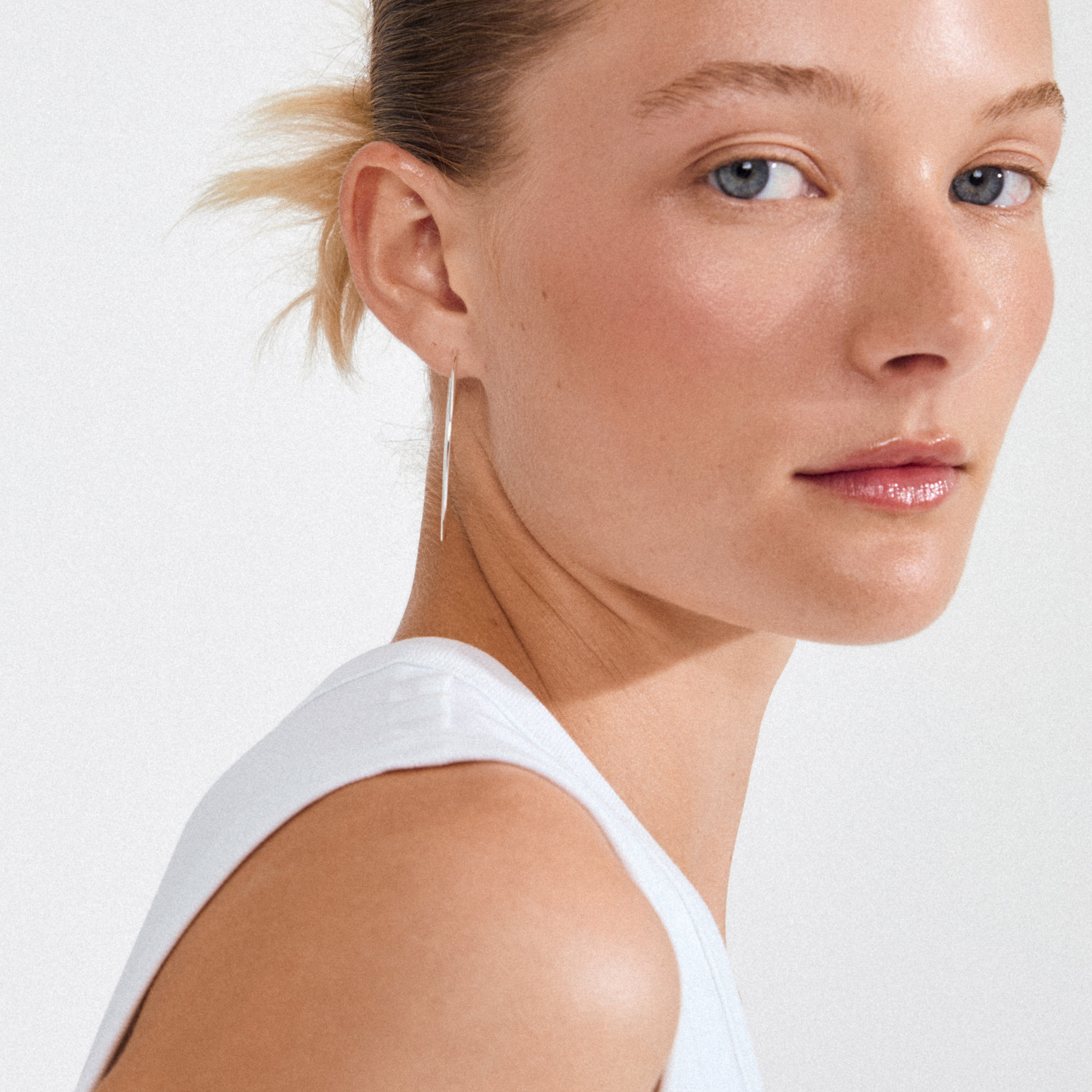 Close-up of a young woman wearing a white tank top, showcasing SANNE large silver-plated hoop earring, emphasizing timeless elegance and modern style by Pilgrim.