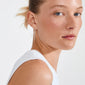 Close-up of a young woman wearing a white tank top, showcasing SANNE large silver-plated hoop earring, emphasizing timeless elegance and modern style by Pilgrim.
