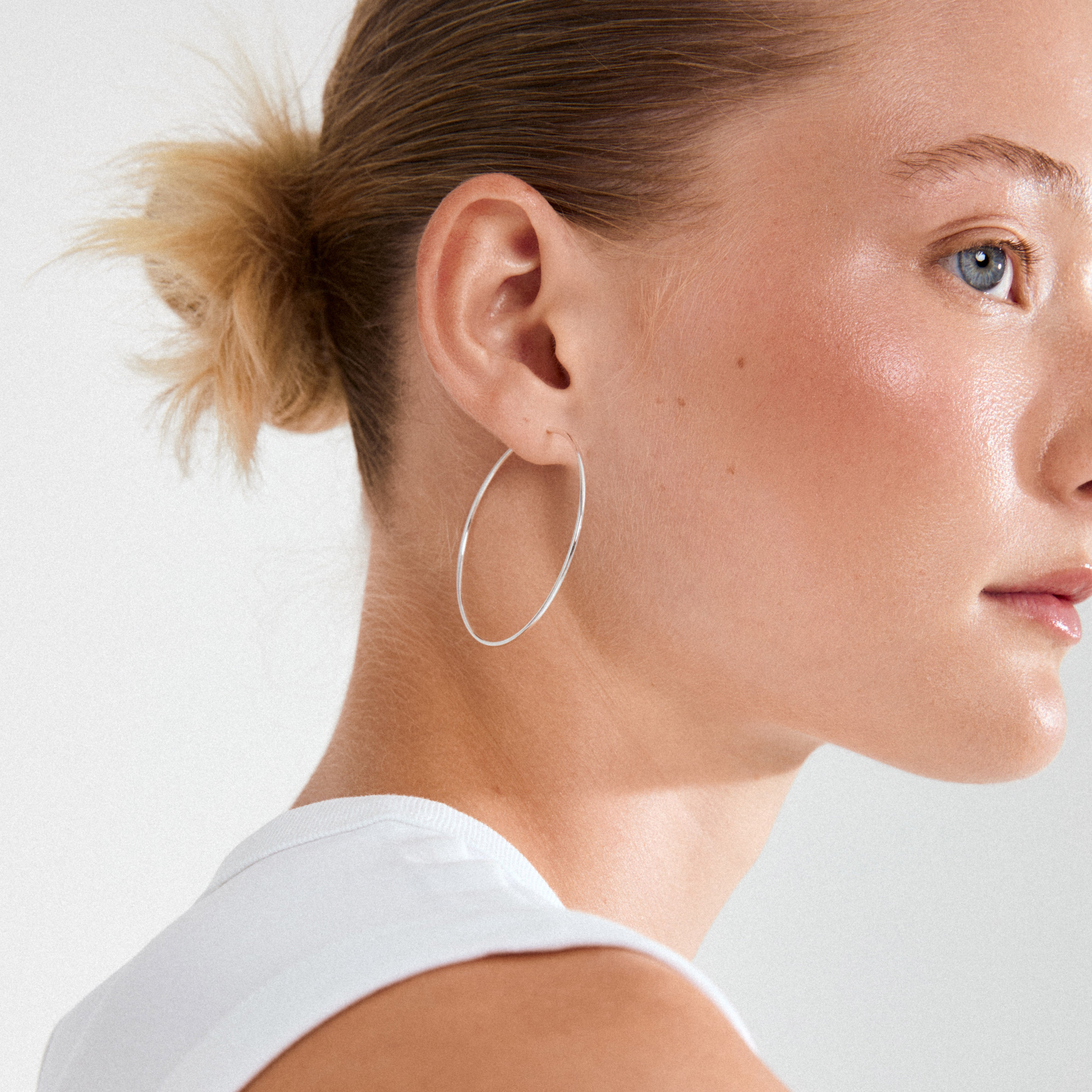 SANNE large hoop earrings, silver-plated, adorn a young woman’s ear, showcasing their timeless elegance as a versatile fashion staple.