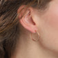 BELLA semi-hoop earrings rosegold-plated, showcased on a woman's ear, highlighting their polished, tribal-inspired design and medium-sized, glowing hoops as a fashion accessory.