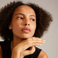 Woman with curly hair, hand on chin, wearing a LULU stack ring gold-plated by Pilgrim, showcasing its elegance and stackable design.