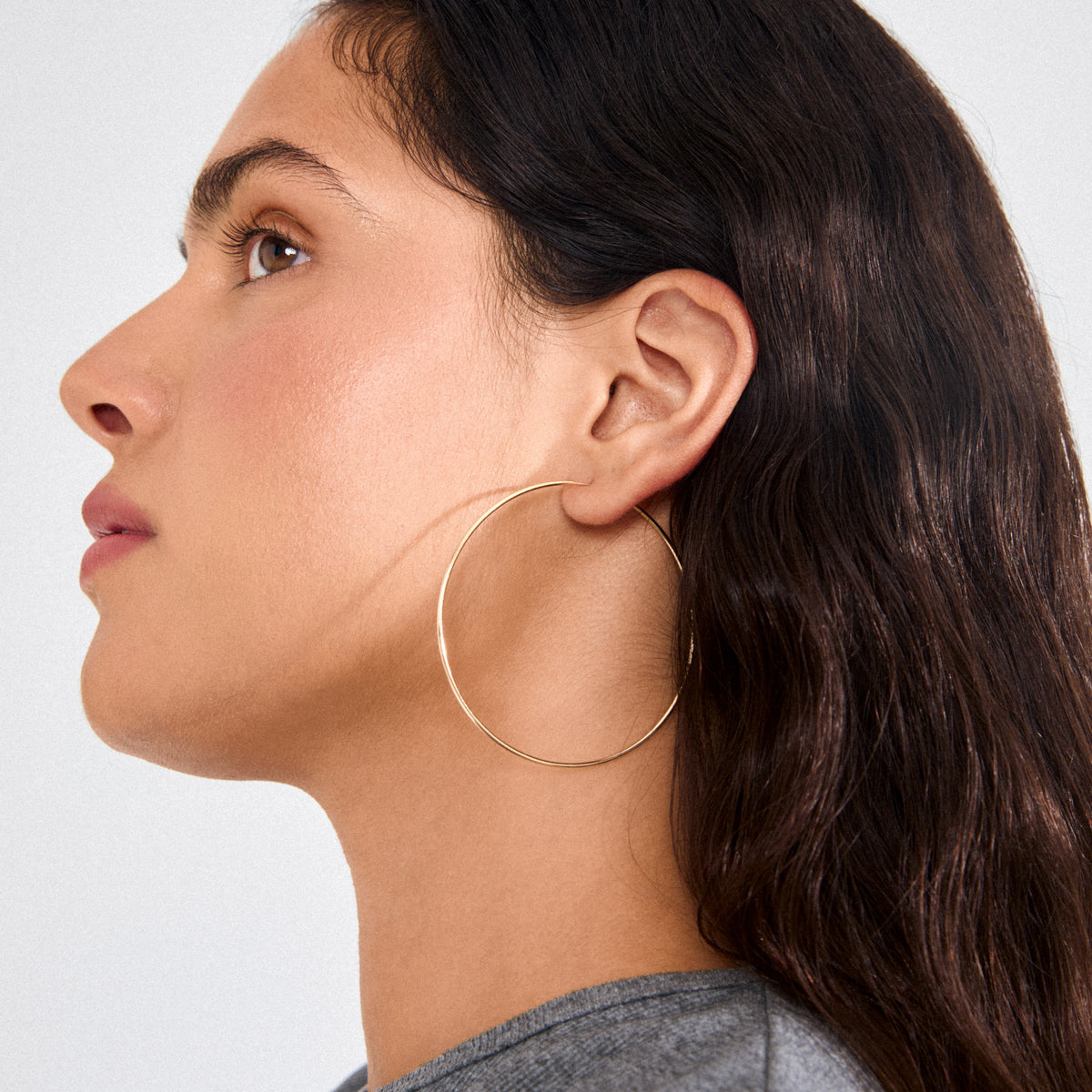 Young person wearing a large, gold-plated SANNE X-large hoop earring, showcasing its slim, lightweight design and 60 mm oversized diameter.
