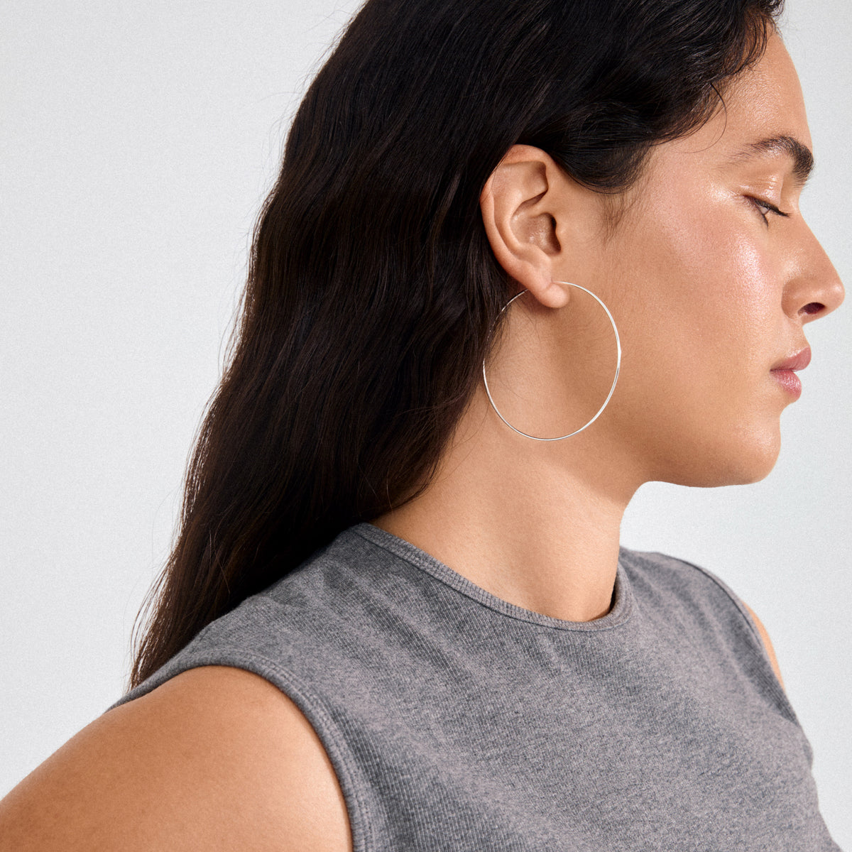 Young person wearing SANNE X-large hoop earrings silver-plated; sleek, lightweight design showcased in side profile, emphasizing the oversized 60 mm diameter for a bold, stylish statement.