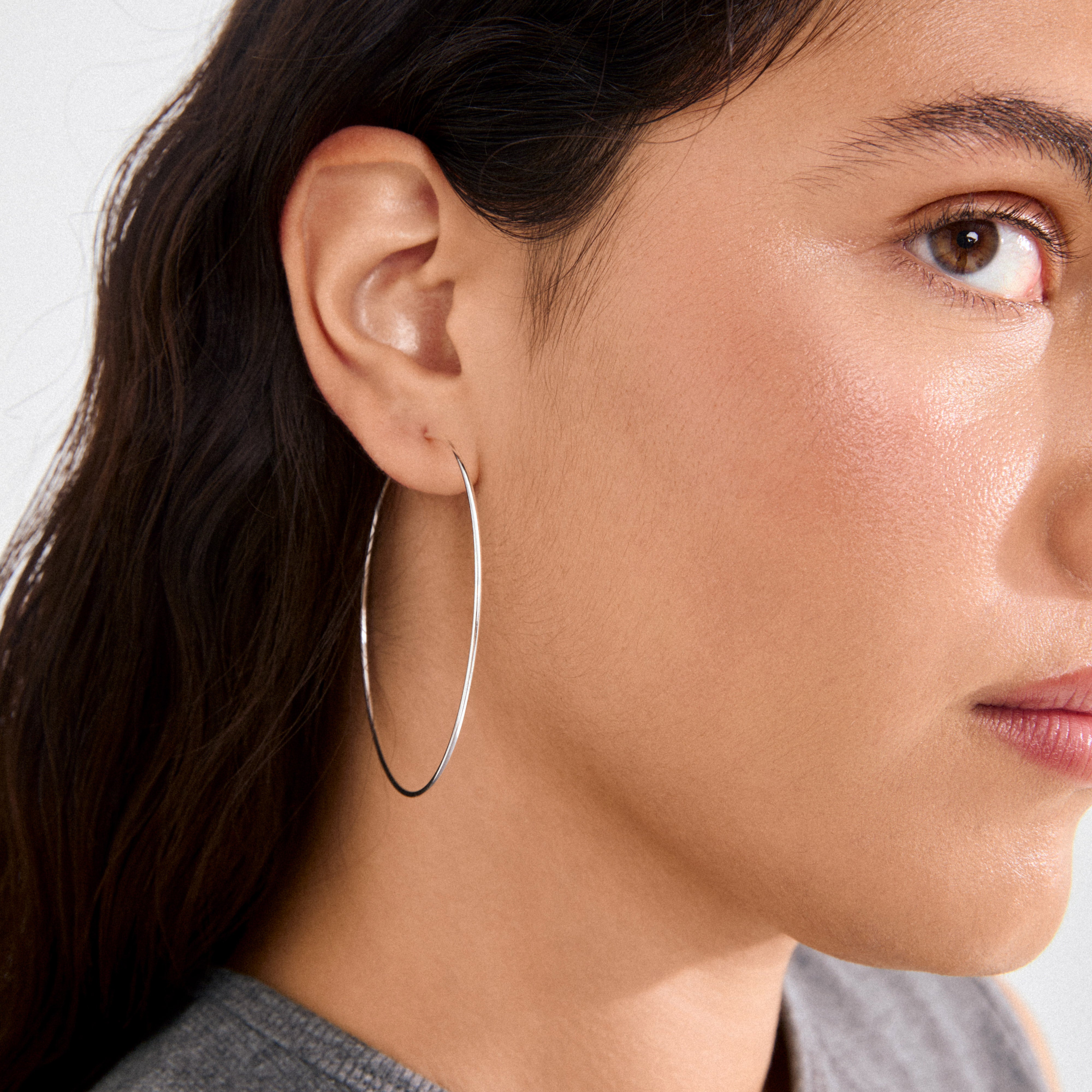 Profile view showcasing the SANNE X-large silver-plated hoop earring, highlighting its sleek, lightweight design with a 60 mm diameter on a woman's ear.