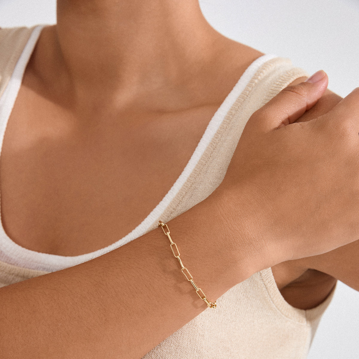 Person wearing a light beige tank top with the RONJA bracelet, featuring sleek, rectangular gold-plated links in an airy cable chain on their wrist.