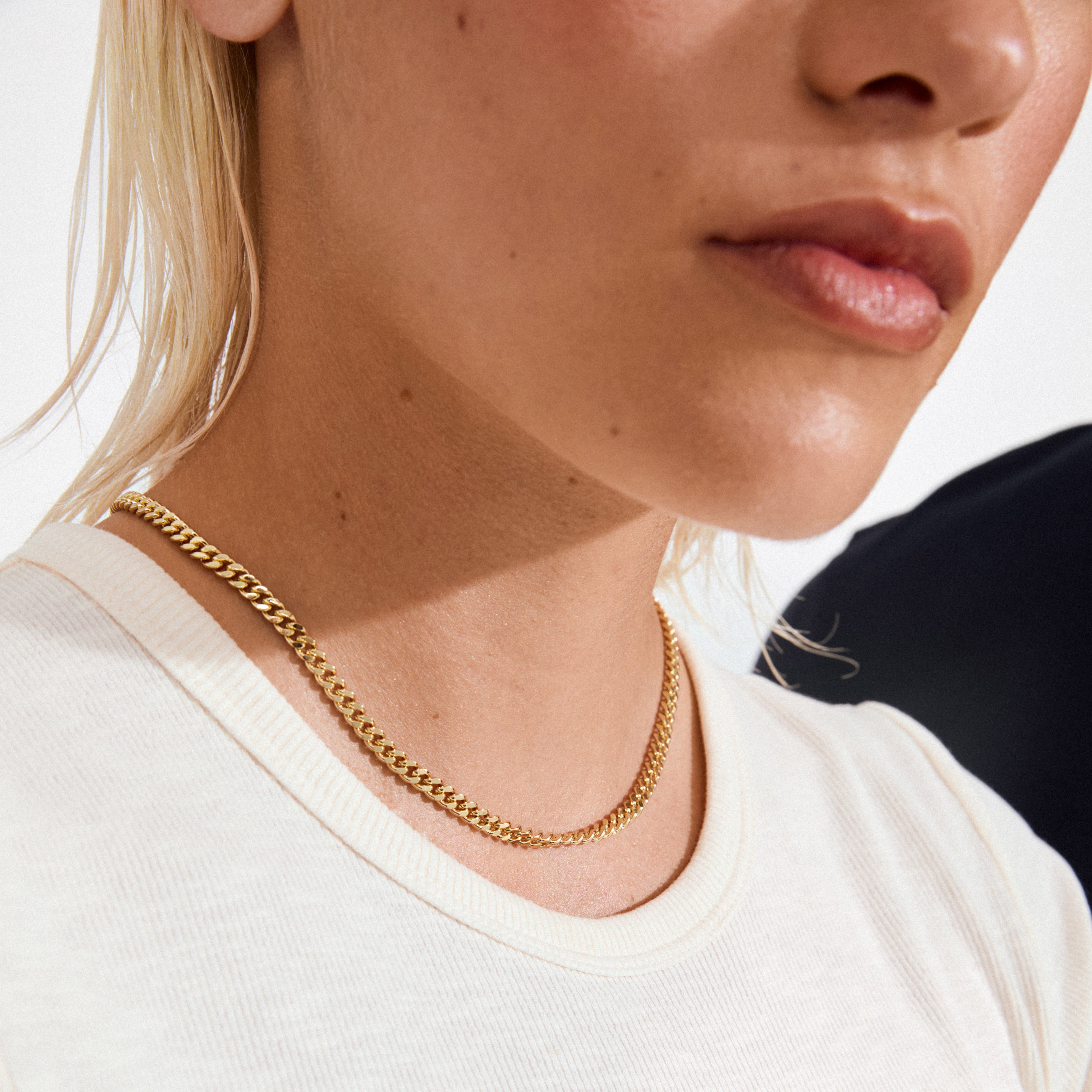 FUCHSIA curb chain necklace in gold-plated finish on a white rib-knit T-shirt, highlighting its semi-chunky, faceted links and stylish, versatile design.