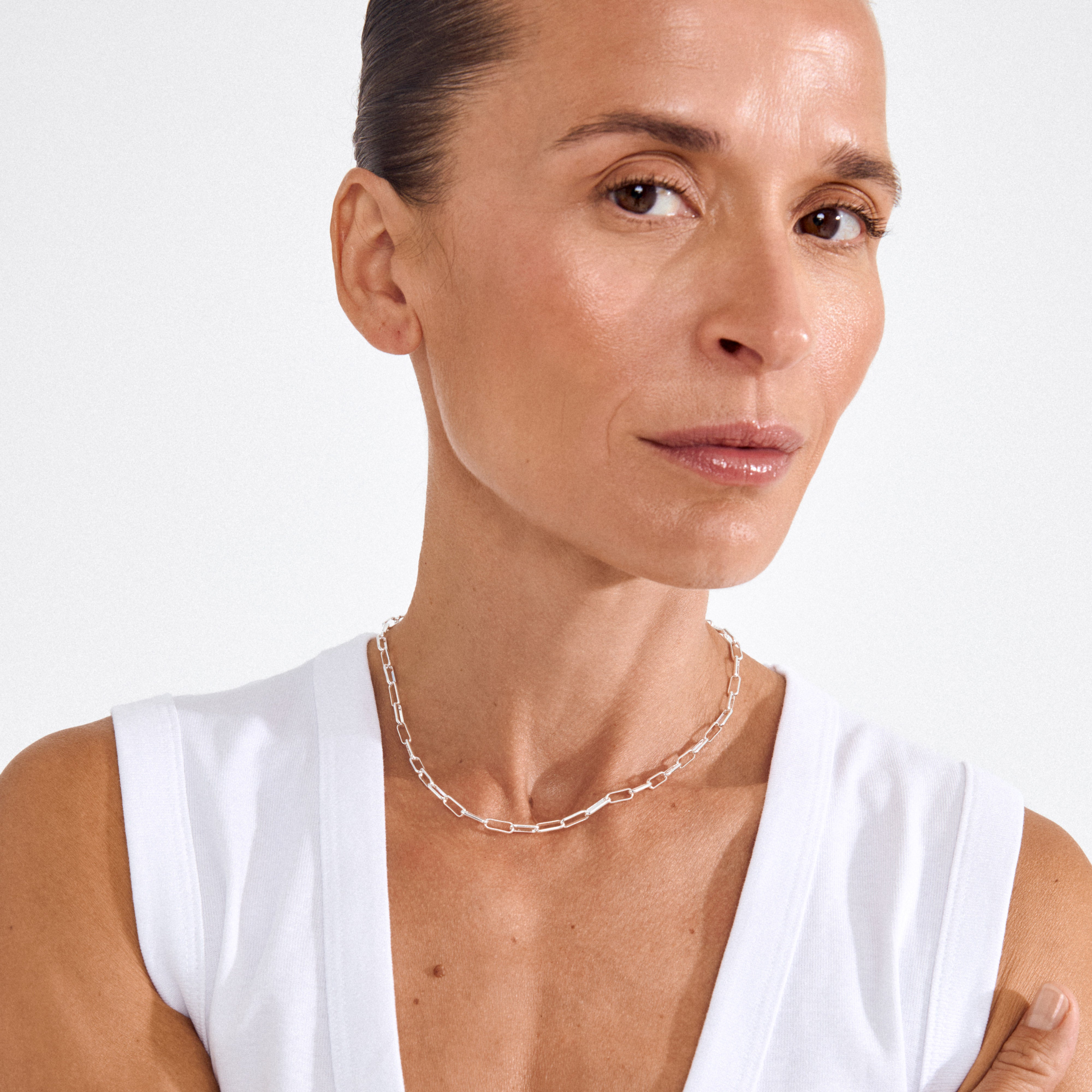 Woman wearing RONJA necklace silver-plated, featuring sleek rectangular links in a contemporary cable chain, accentuating a minimalist, stylish look against a light background.