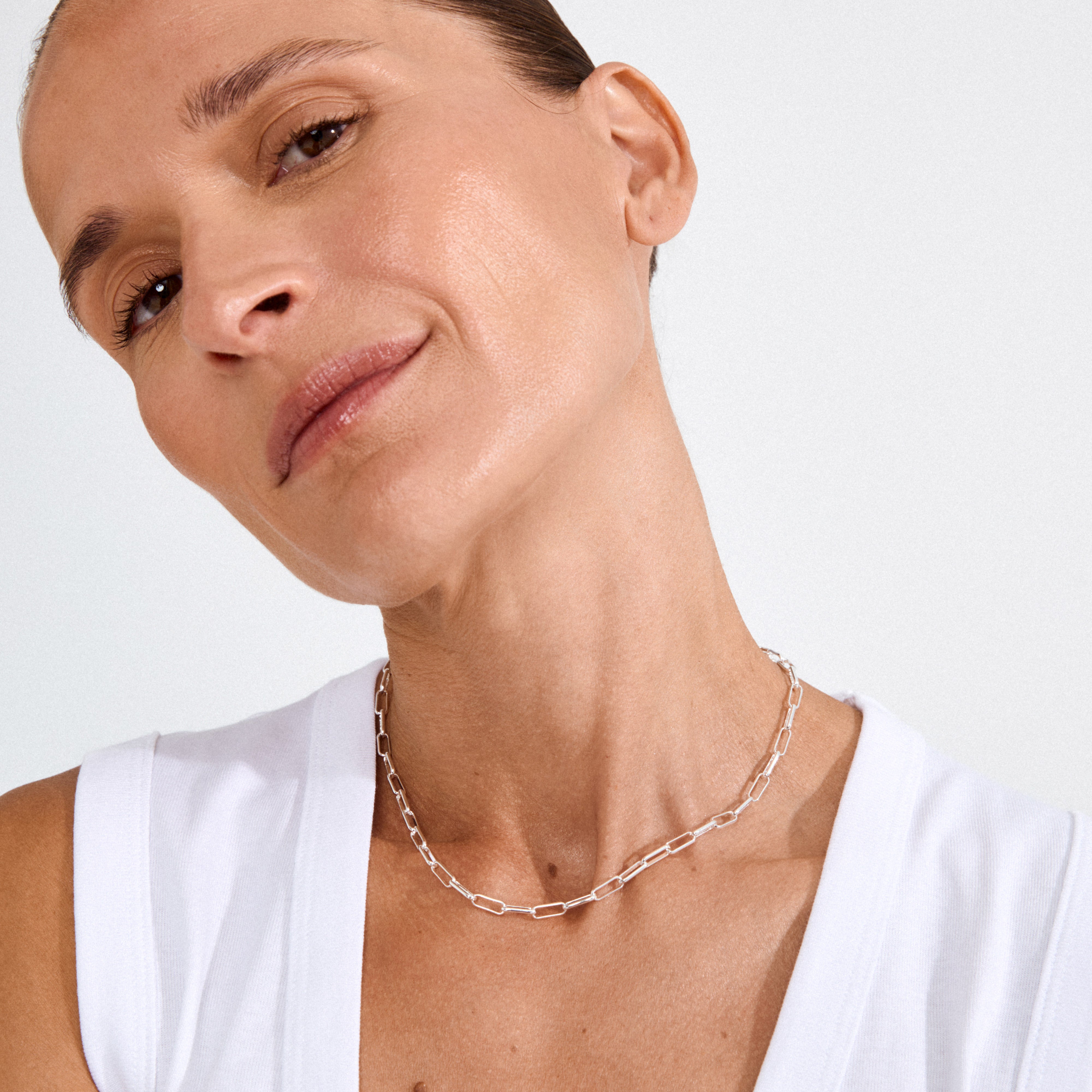 Woman wearing the RONJA necklace, a silver-plated cable chain with rectangular links, highlighting its contemporary style against a simple white top.