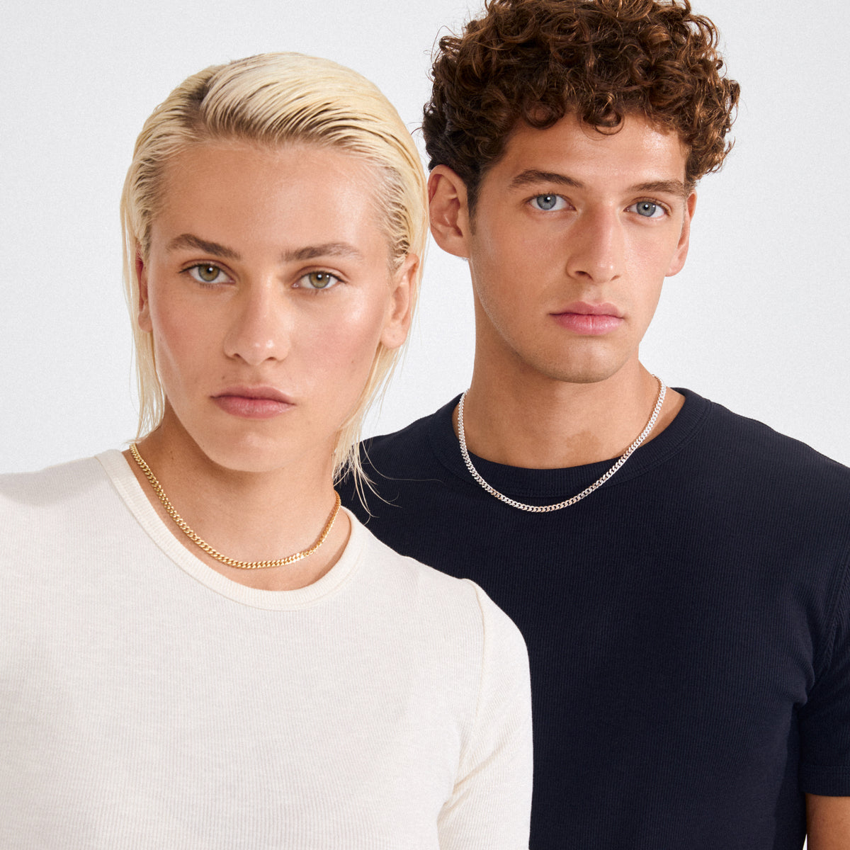 Two young adults wearing Pilgrim's FUCHSIA curb chain necklaces, silver-plated with faceted links, showcasing the semi-chunky, timeless style against a light background.