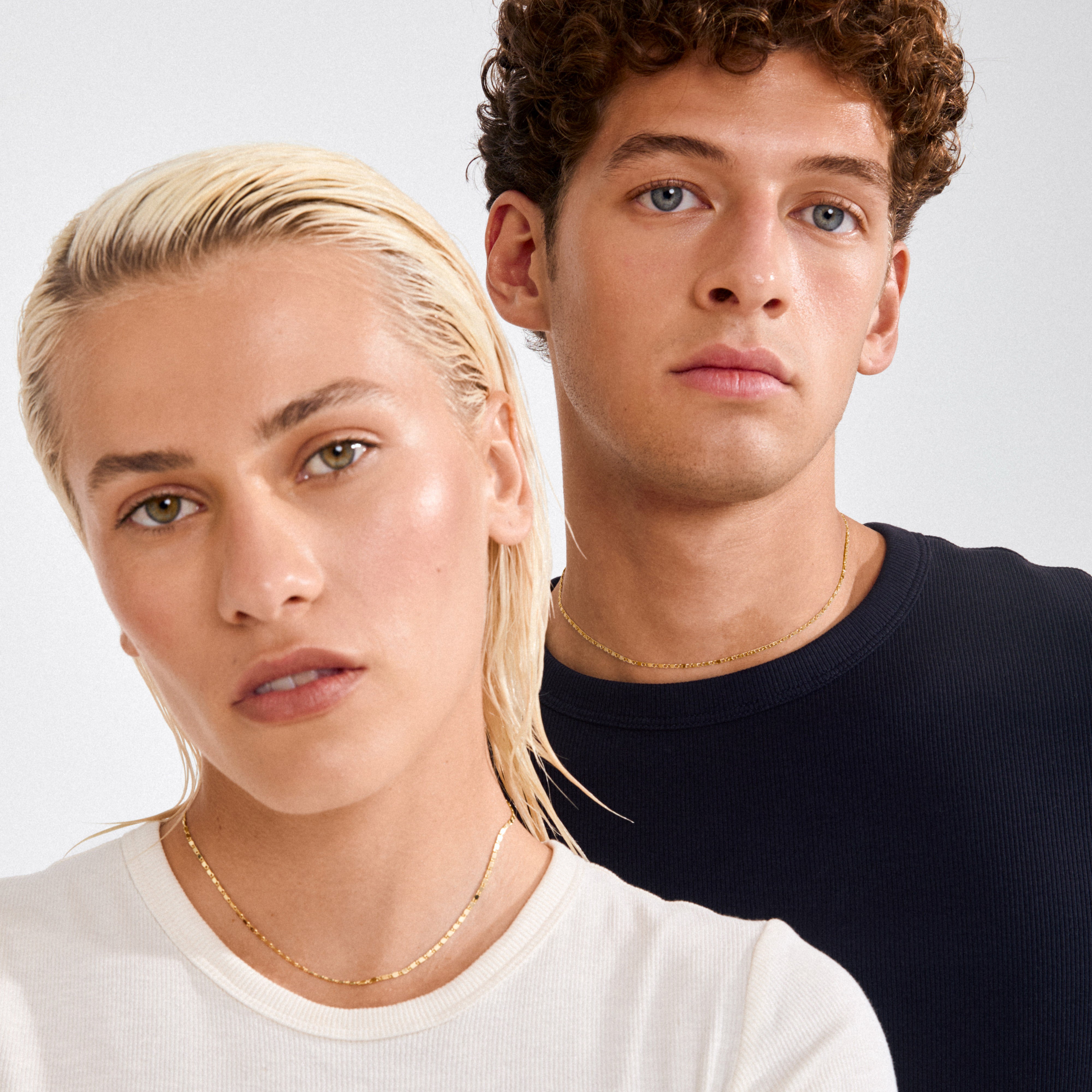 Two young adults wearing Pilgrim's PARISA flat link chain necklace, showcasing its gold-plated, polished links that beautifully reflect light, epitomizing an effortlessly chic style.