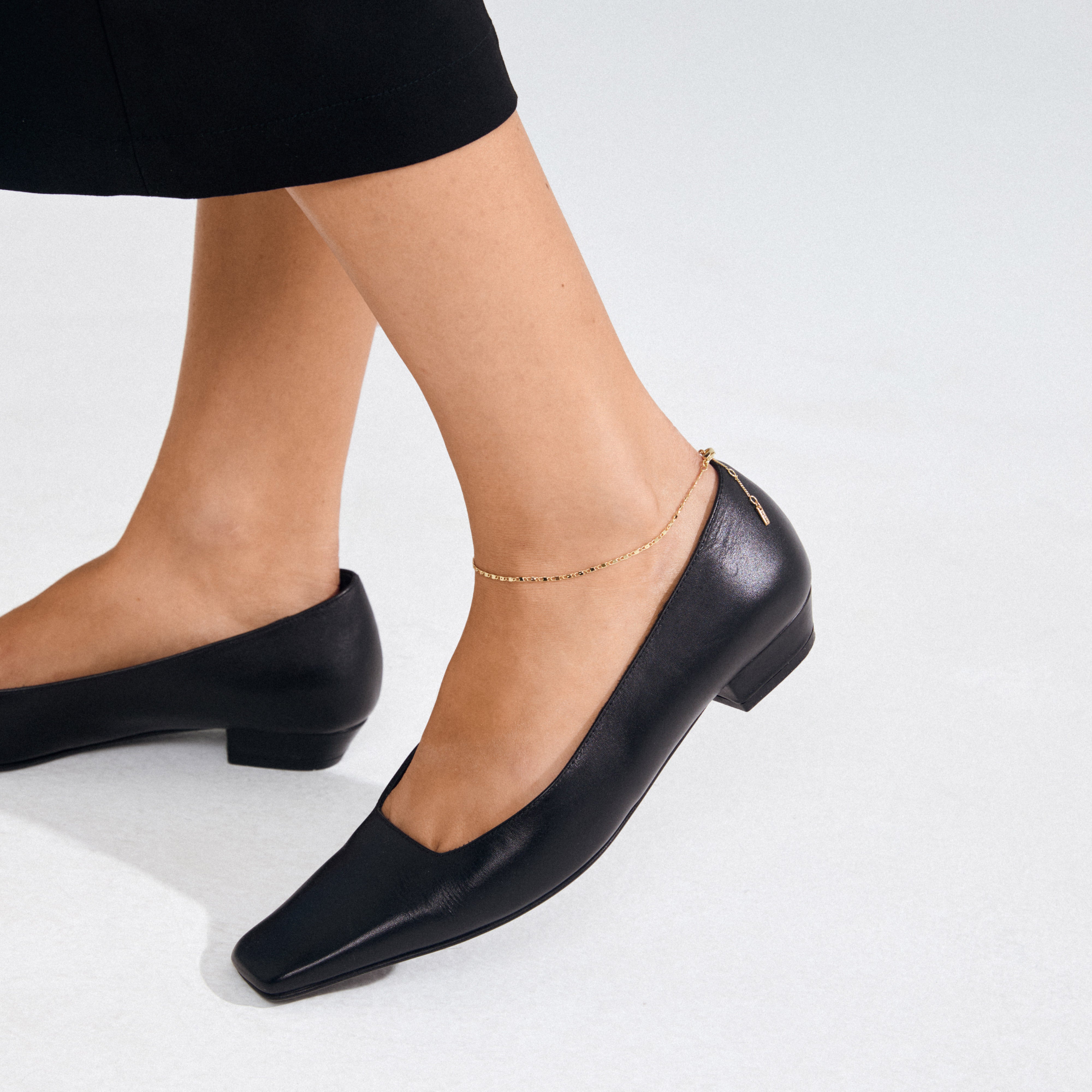 Black leather flats paired with the PARISA flat link ankle chain gold-plated, elegantly highlighting the ankle with its light-catching deco links.