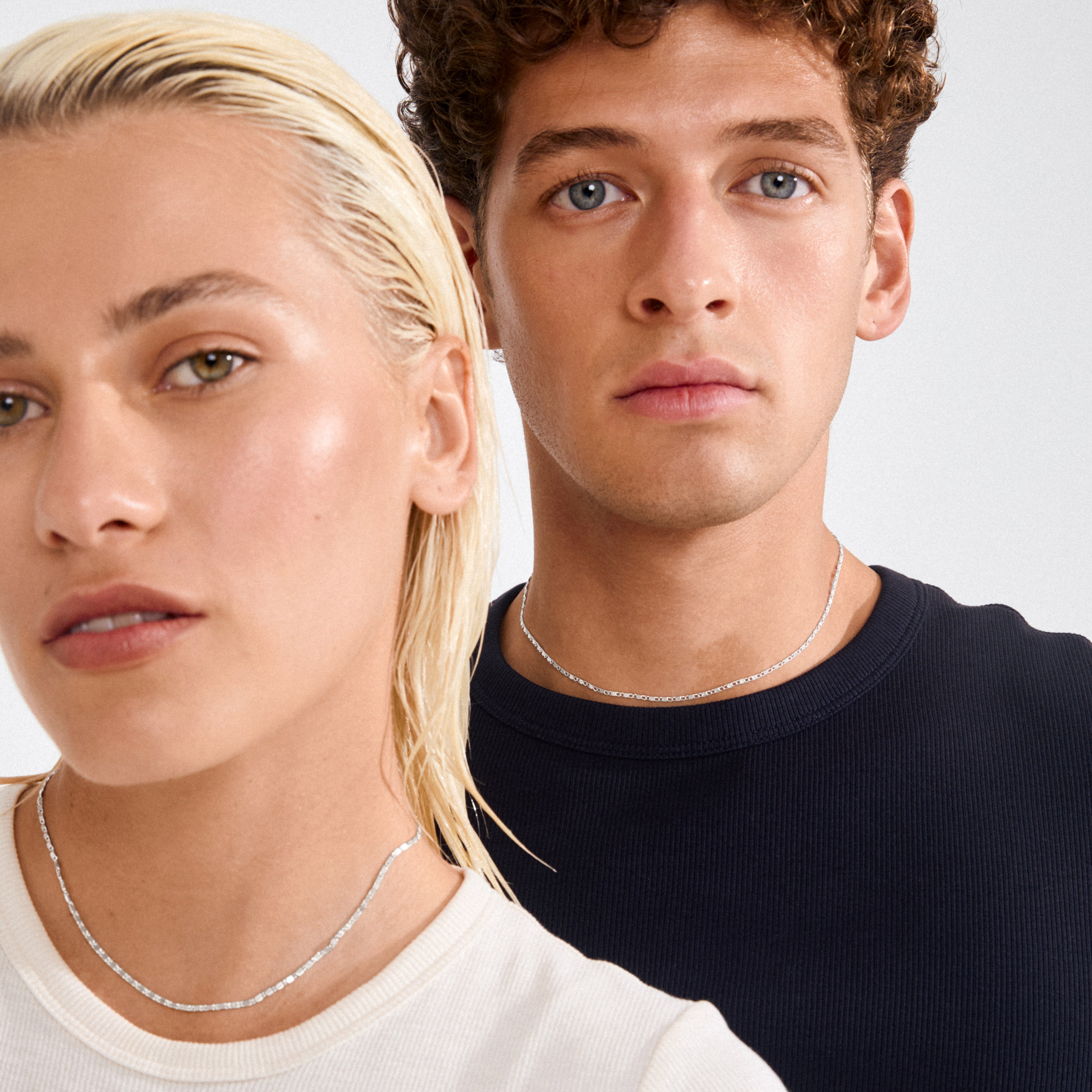 Two models wearing the PARISA flat link chain necklace, silver-plated, highlighting its minimalist, chic design against neutral outfits, embodying Pilgrim's Scandinavian quality and style.