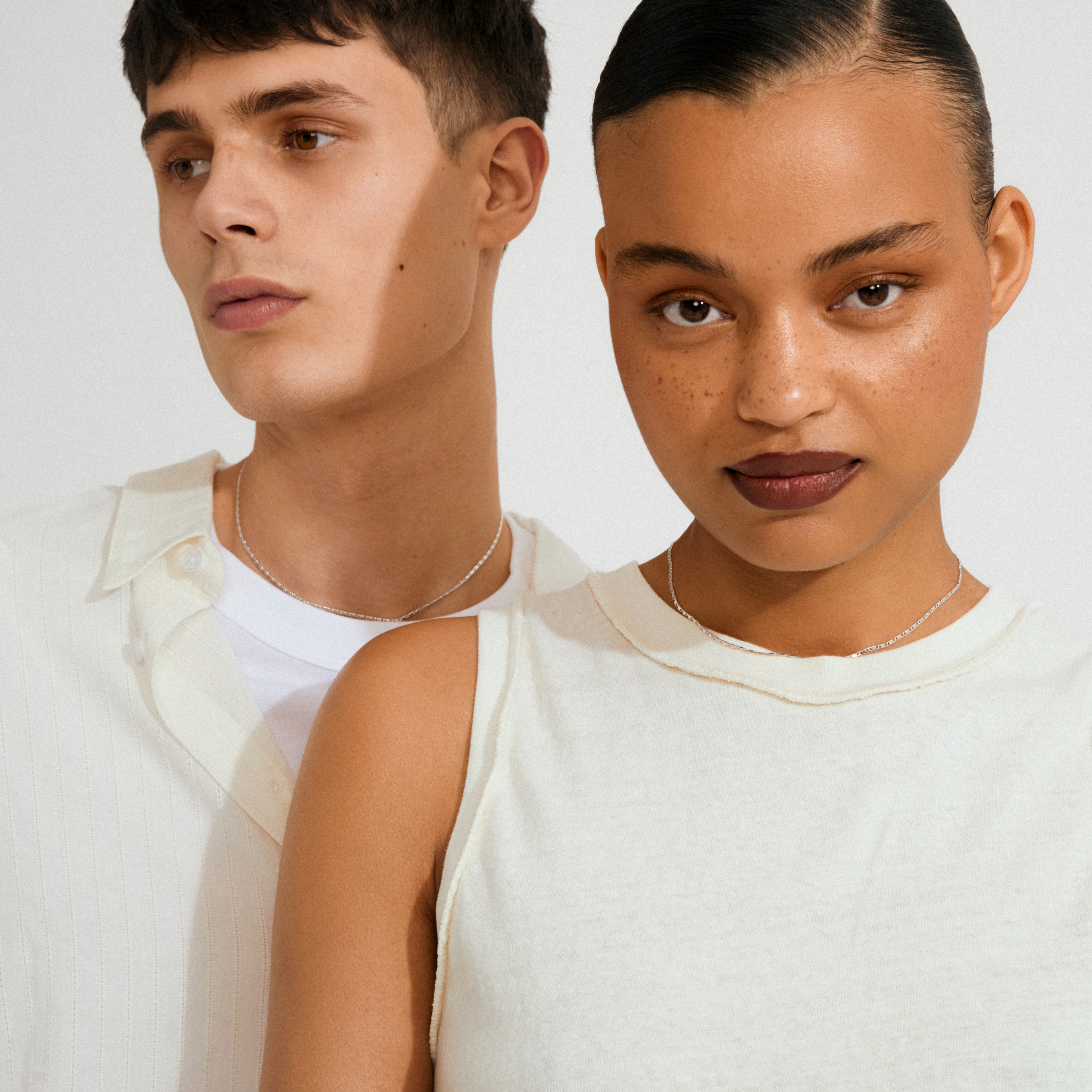 Man and woman wearing PARISA flat link chain necklace silver-plated, showcasing minimalist style in off-white tops, emphasizing Pilgrim's effortlessly chic, Scandinavian-inspired jewelry.