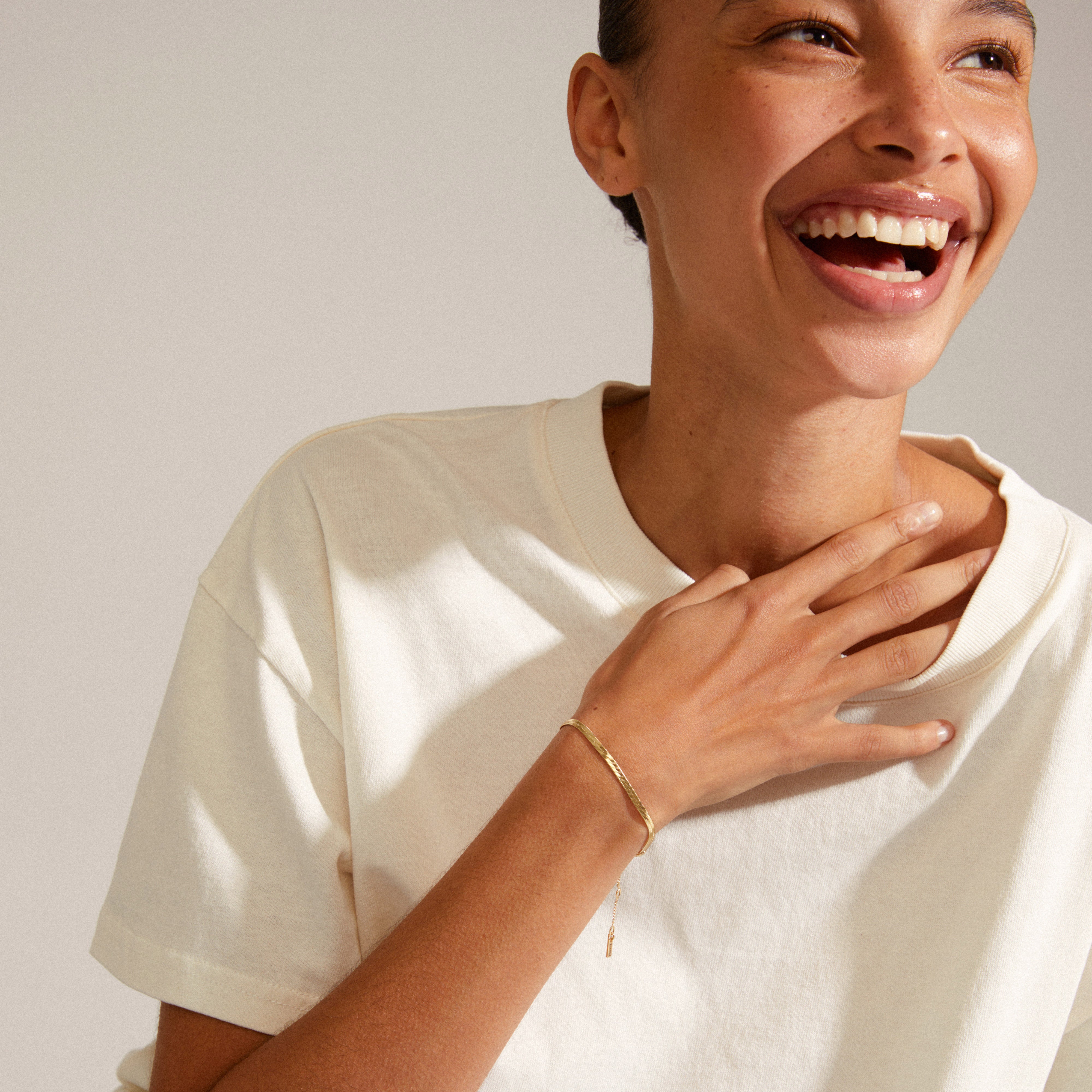 Woman laughing with hand on chest, showcasing the JOANNA flat snake chain bracelet, gold-plated, highlighting its elegant design and stylish extension chain.