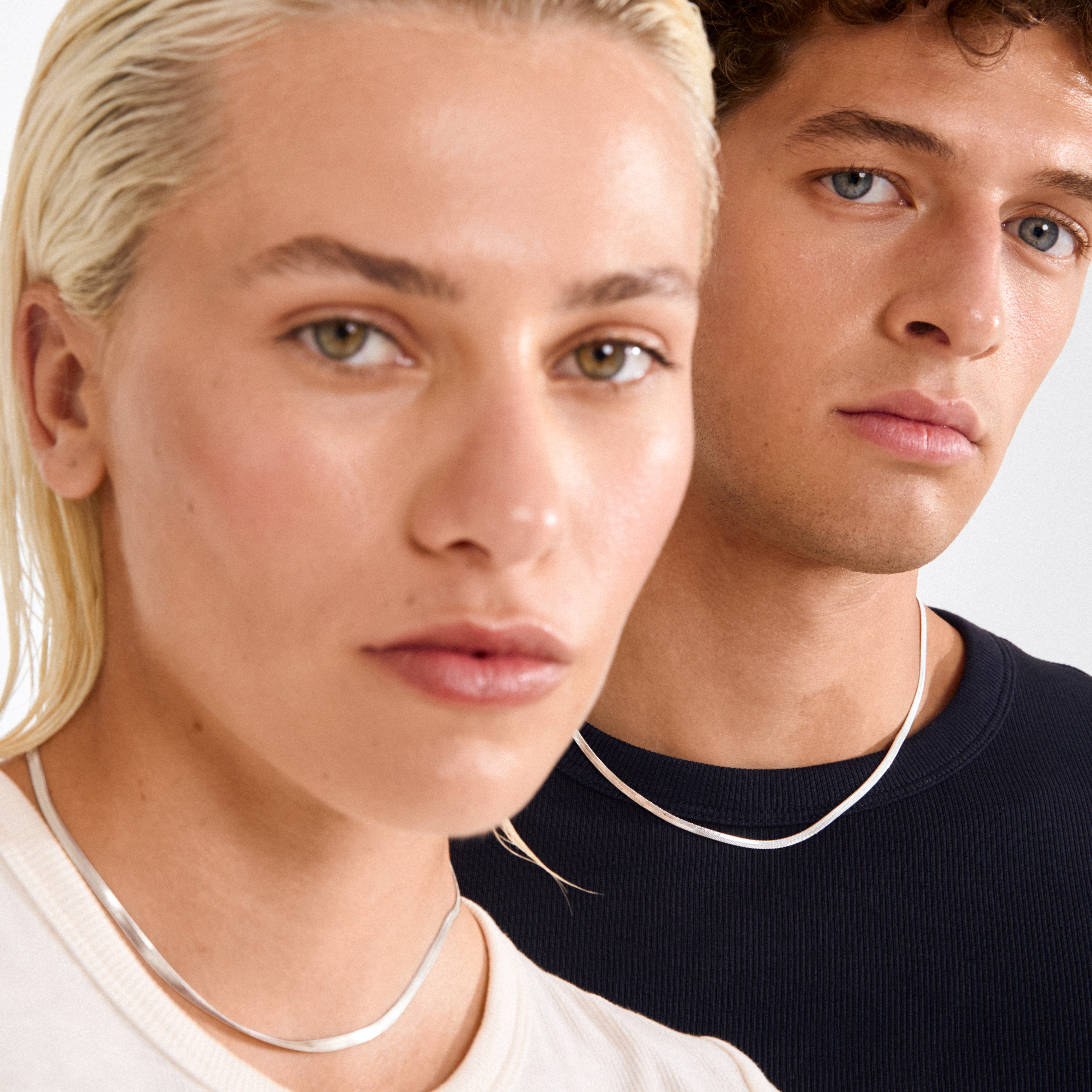 Two young adults wear the JOANNA flat snake chain necklace, highlighting its sleek, polished look, perfect for versatile styling and crafted from recycled materials.