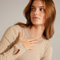 Woman wearing a tan sweater holds her chest, showcasing the LULU organic shaped stack ring gold-plated from Pilgrim, with a handcrafted, wave-inspired design.