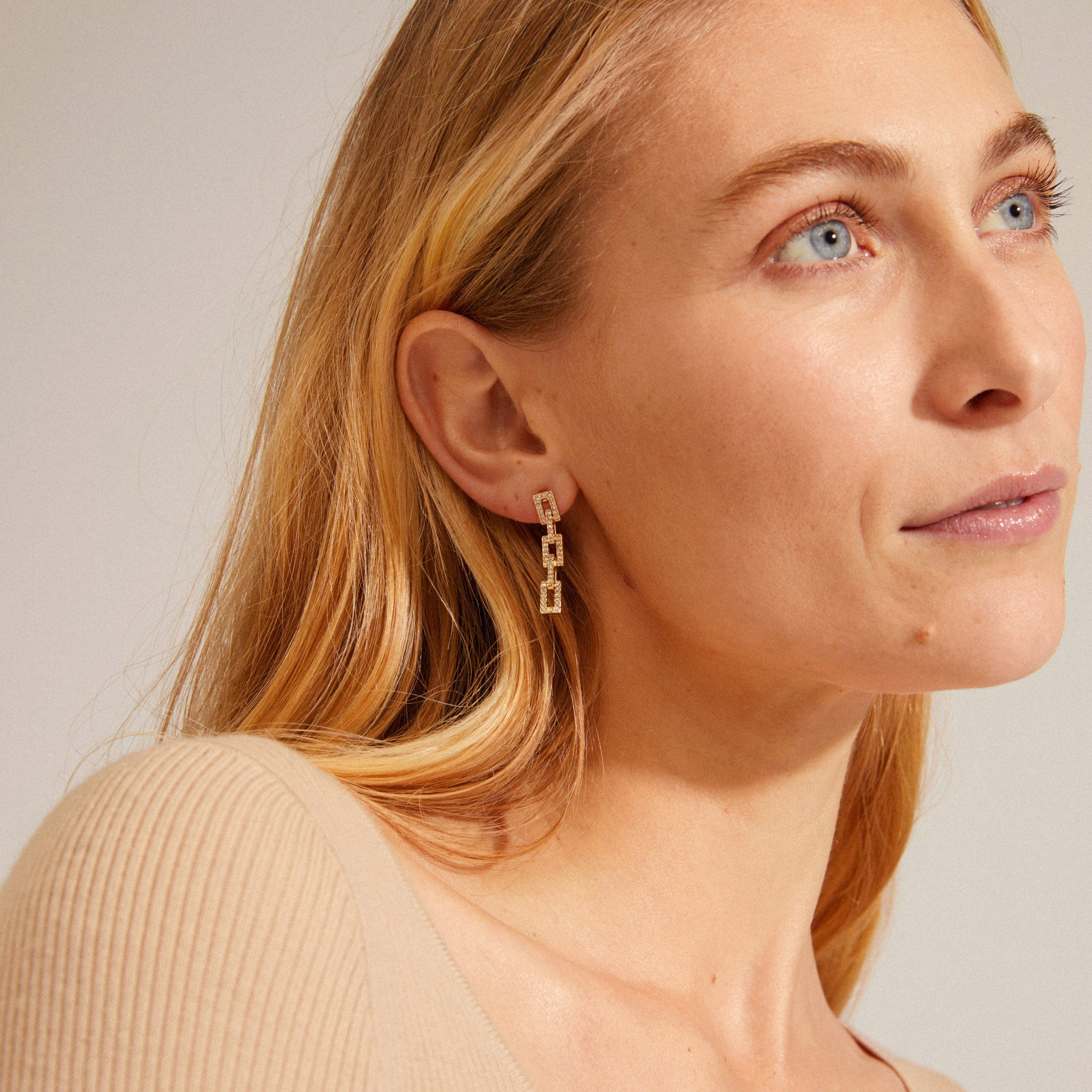 COBY crystal earrings gold-plated: A woman with blonde hair wears elegant gold-plated earrings adorned with sparkling Preciosa crystals, showcasing a retro-inspired design.
