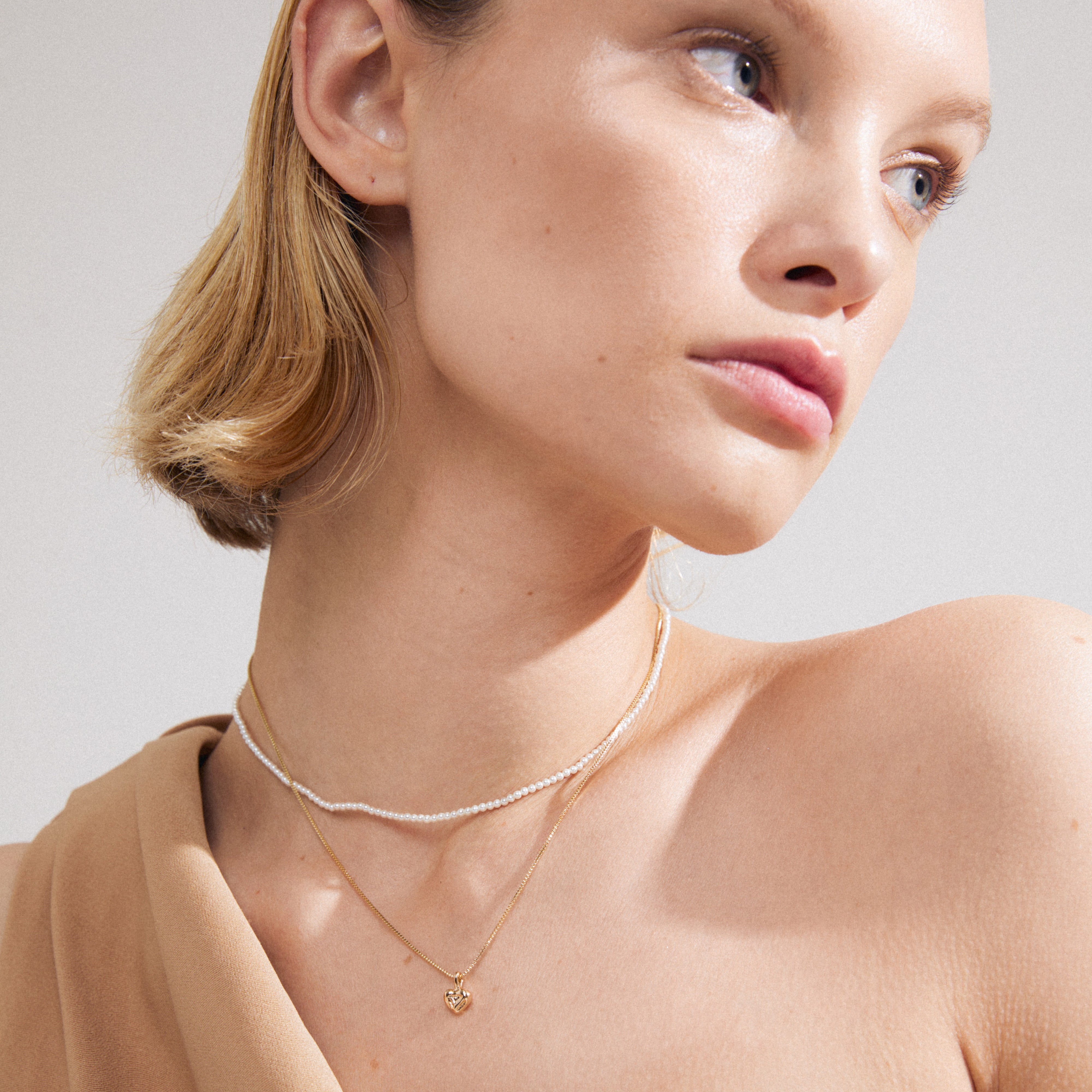 Close-up of a woman wearing the ARLET necklace 2-in-1 set, featuring a gold-plated box chain with a heart and a pearl chain from Pilgrim.