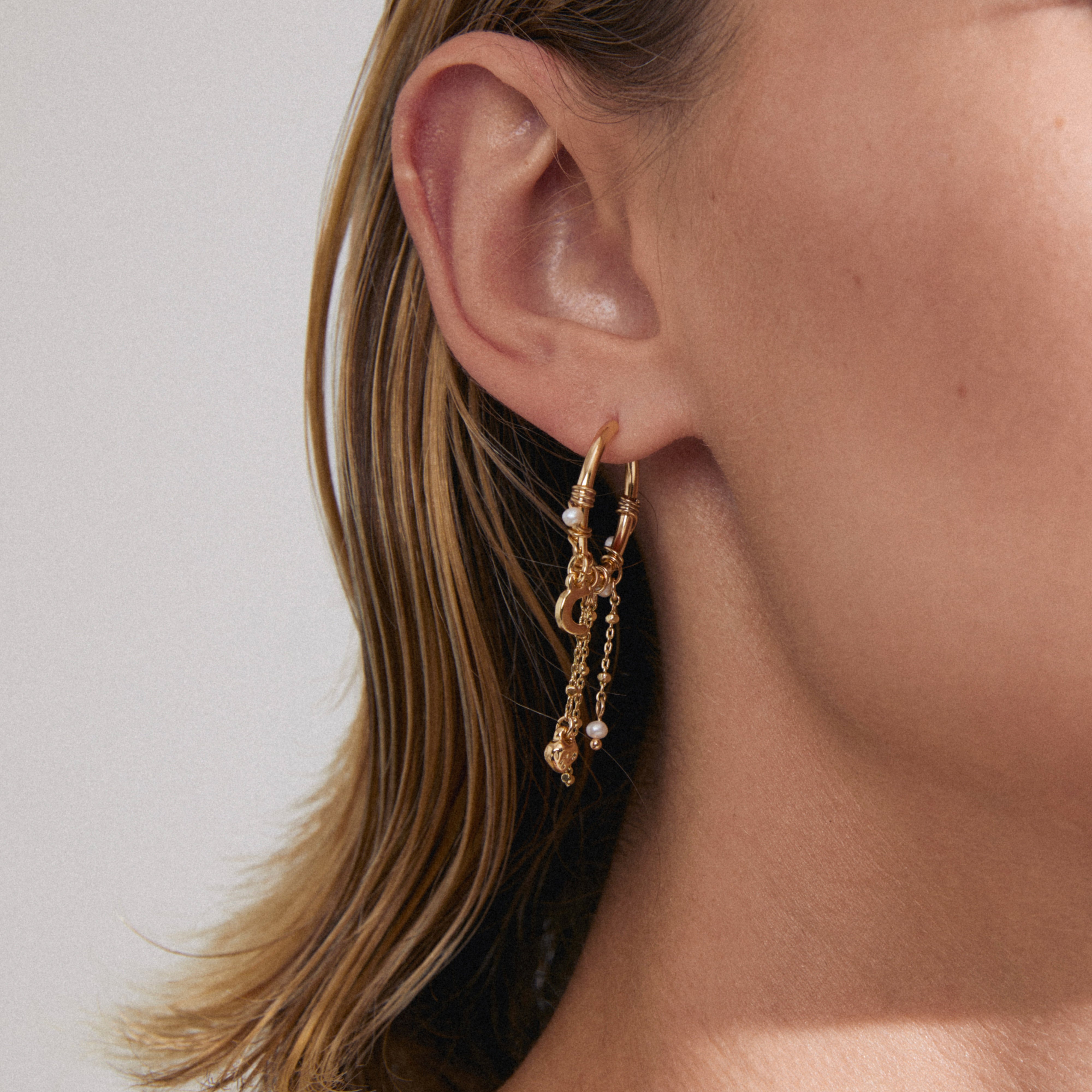 ARLET gold-plated hoop earrings by Pilgrim on ear; one plain, one with wire, pearls, dangling chains, charms, adding a boho-lux romantic flair.