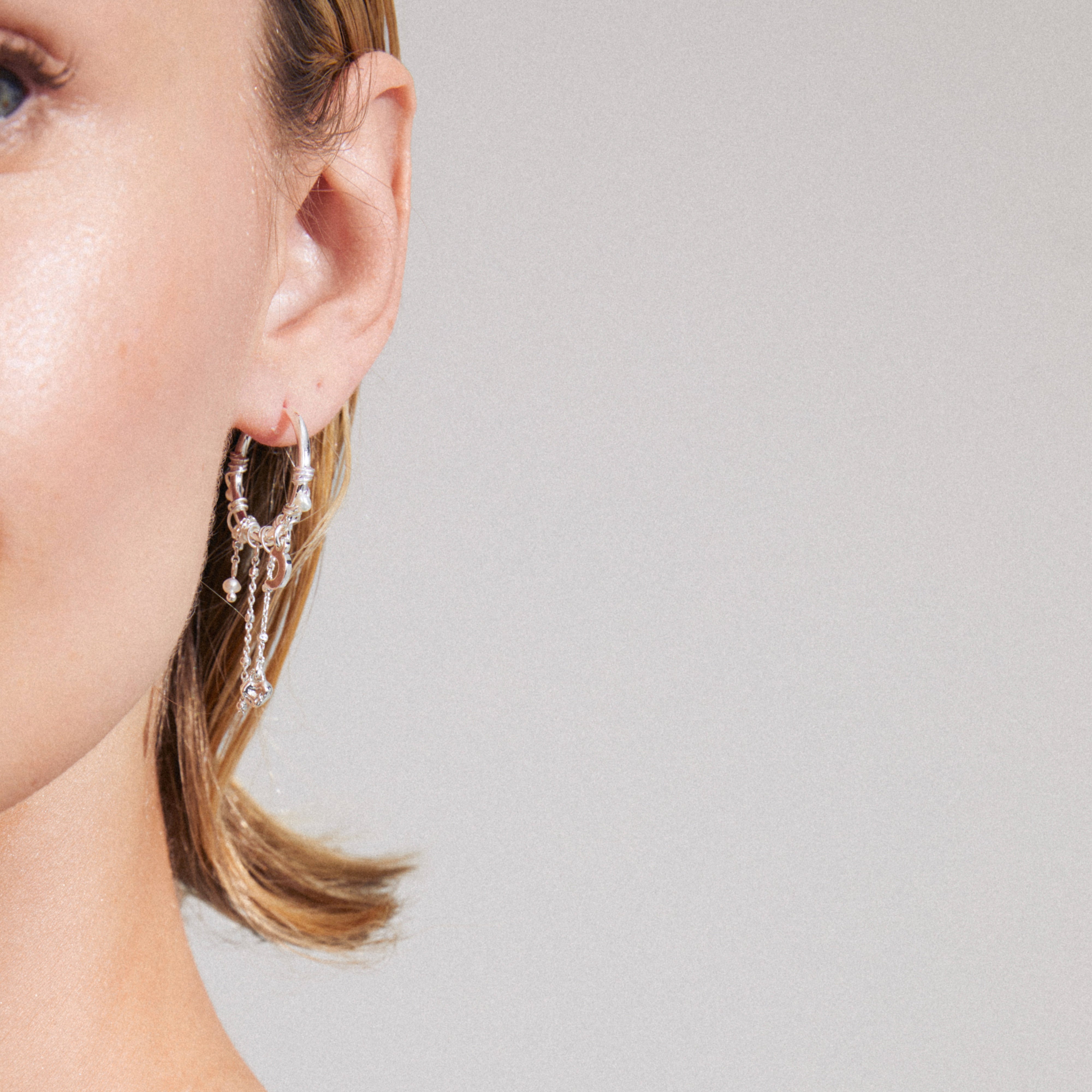 ARLET earrings silver-plated on ear, featuring freshwater pearls, Preciosa crystals, and moon and heart charms, showcasing a boho-lux aesthetic from Pilgrim.