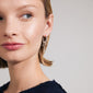 Silver-plated ARLET hoop earrings featuring freshwater pearls, Preciosa crystals, moon pendants, and hearts, worn by a woman with short blonde hair.